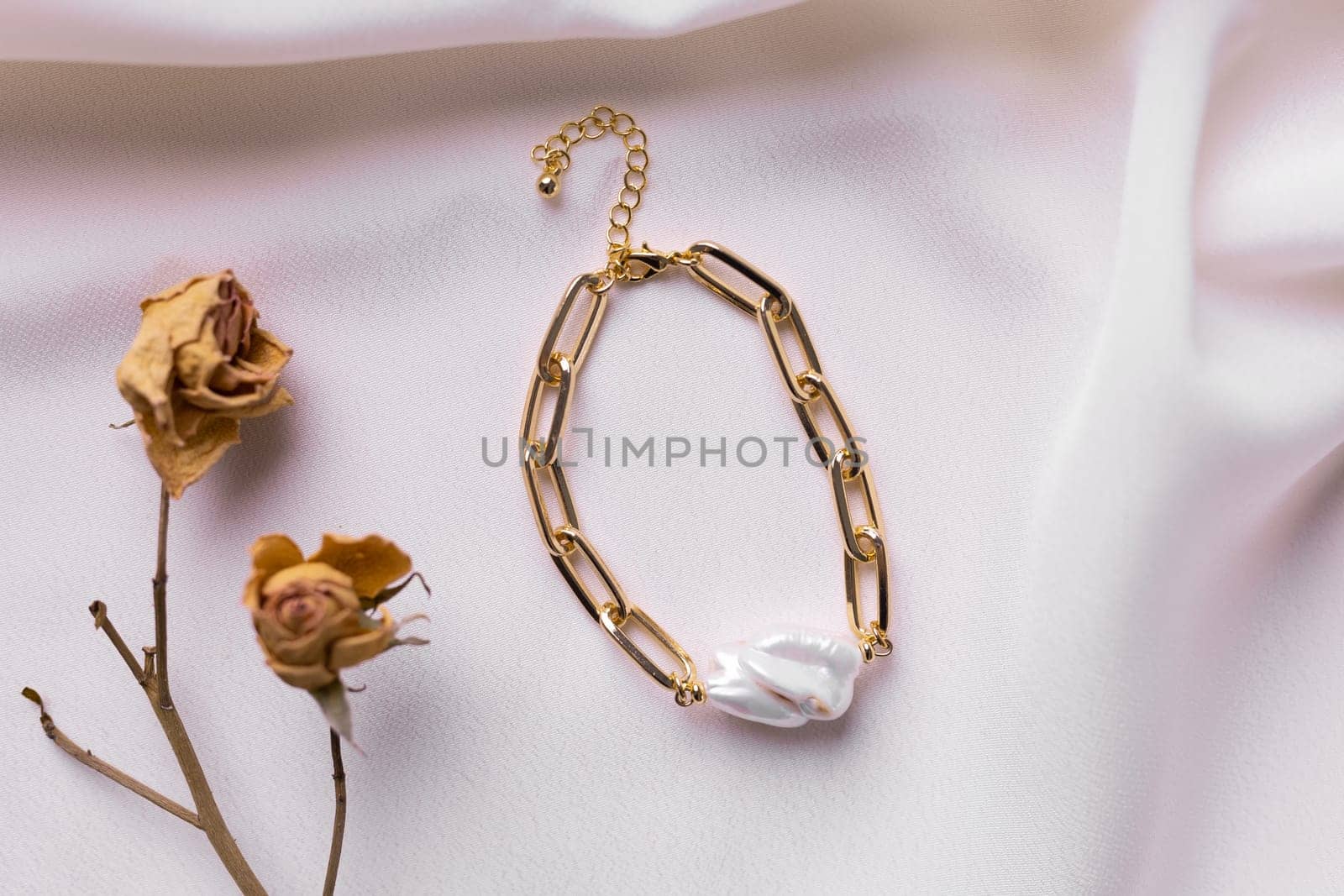 Jewelry on satin fabric with gold pearl bracelets and dry flowers elements. Handmade bijouterie and natural aesthetics in fashion.