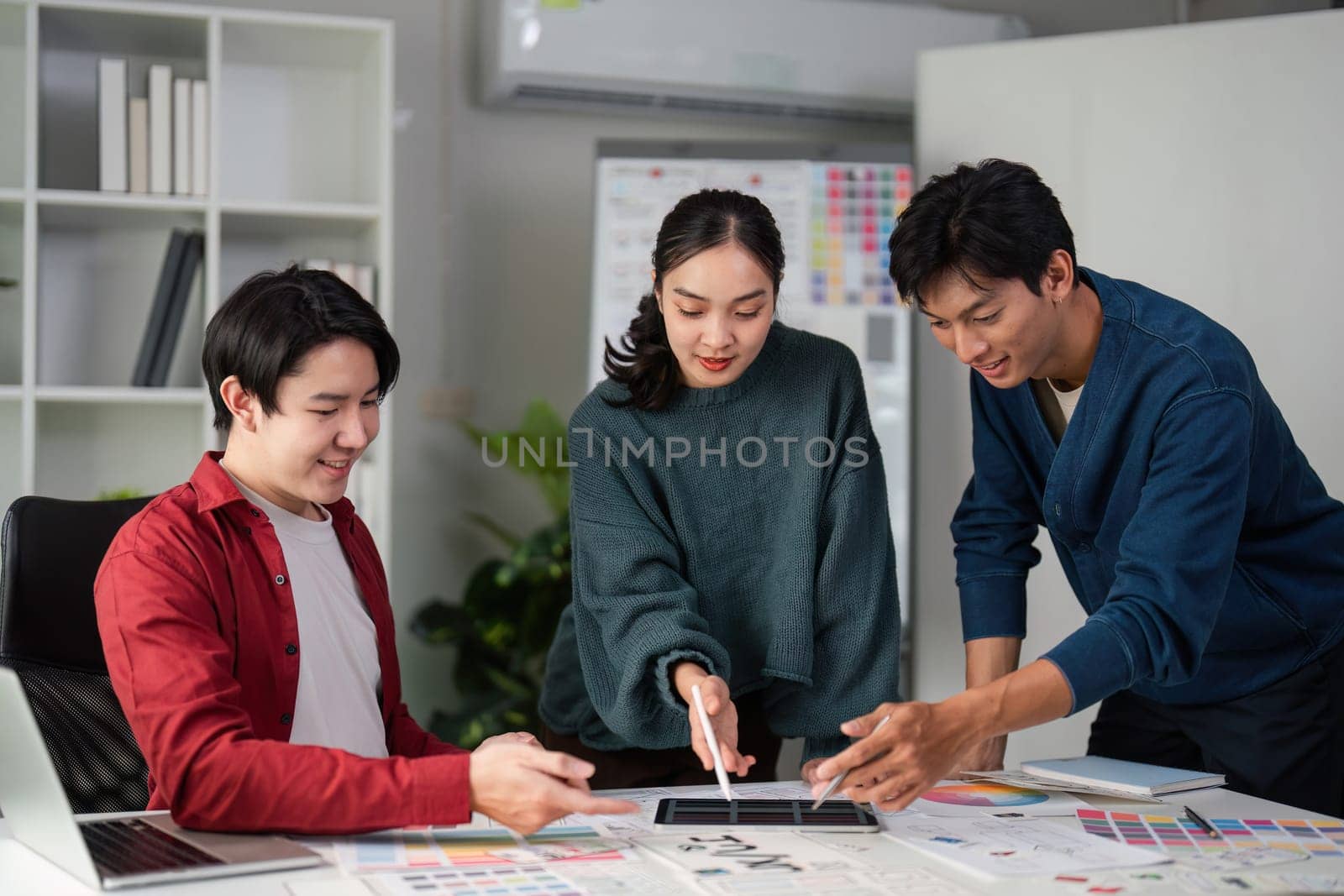 A group of designers brainstorms while analyzing color selections and mockups, illustrating their teamwork and creativity in a visually stimulating environment.