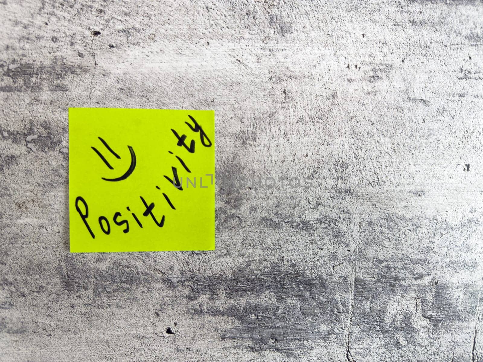 Sticky note displaying the word Positivity along with smiley face on a textured grey surface, embodying the spirit of optimism and the importance of a positive attitude in everyday life