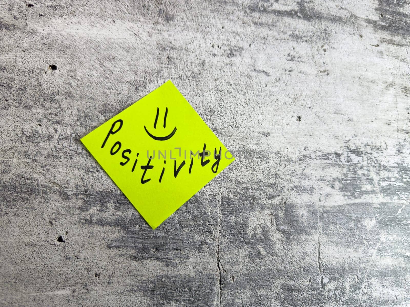 Bright yellow sticky note shaped as diamond featuring the word Positivity and smiley face on textured grey background, symbolizing cheerful mindset and the power of positive thinking in daily life