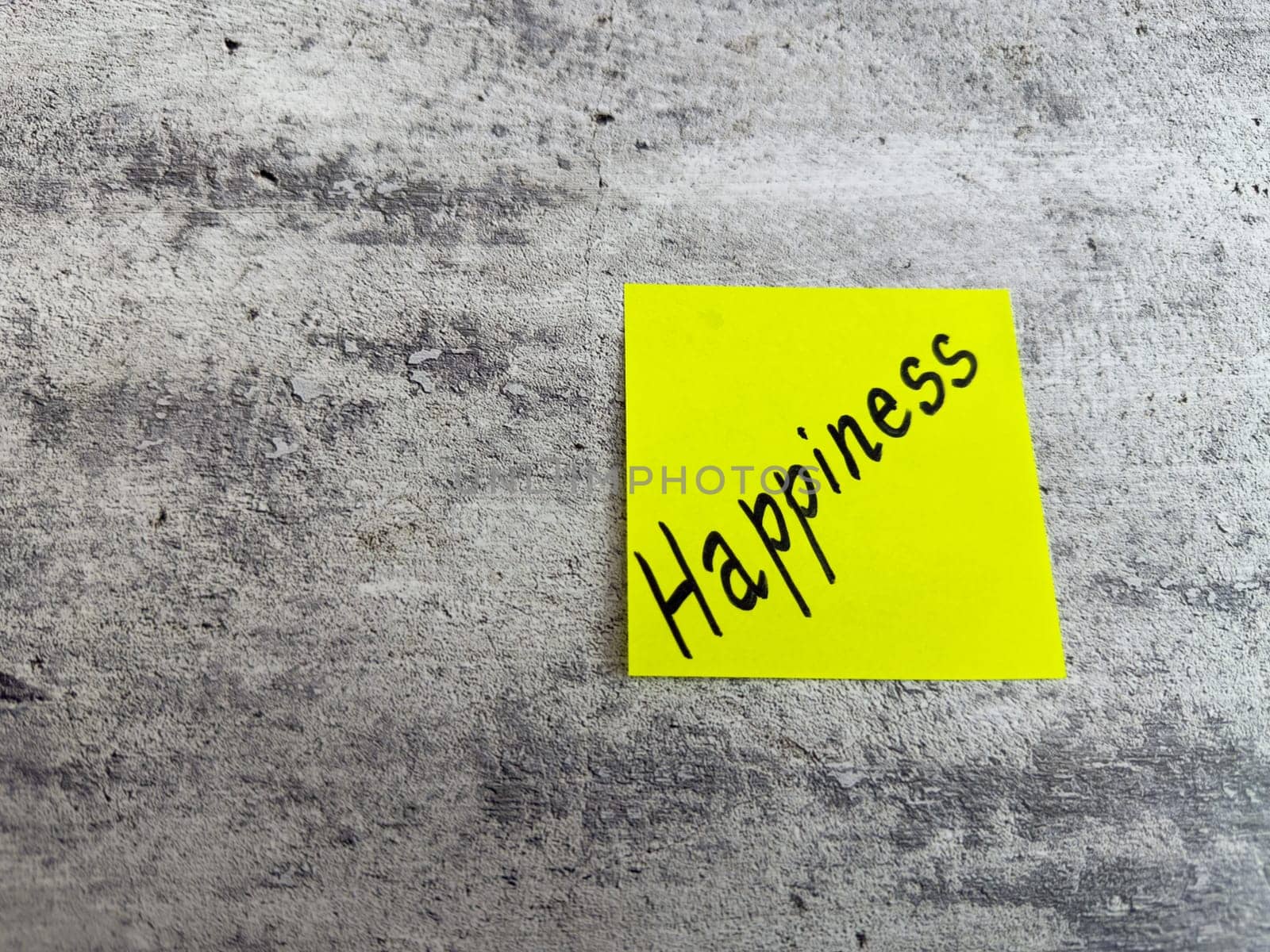Vivid yellow sticky note displaying the word Happiness against a textured grey background, symbolizing the importance of joy and positivity in everyday experiences and personal growth