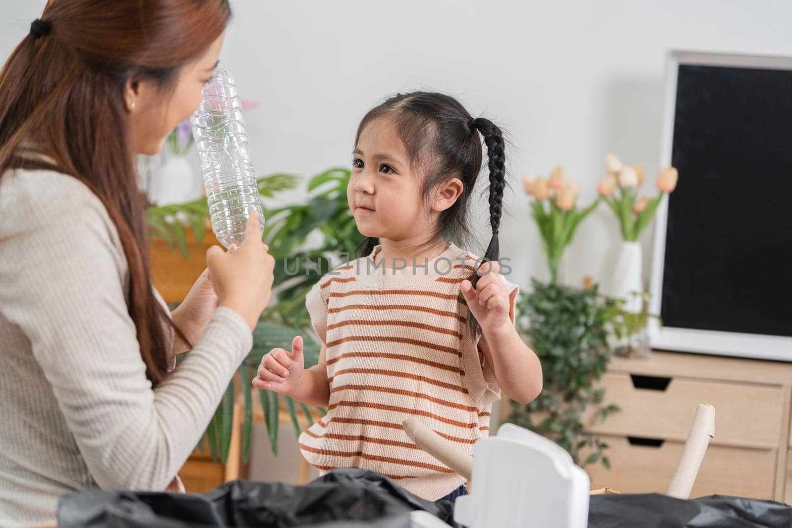 A mother demonstrates how to recycle plastic bottles while her daughter curiously observes, fostering a love for eco-friendly practices.