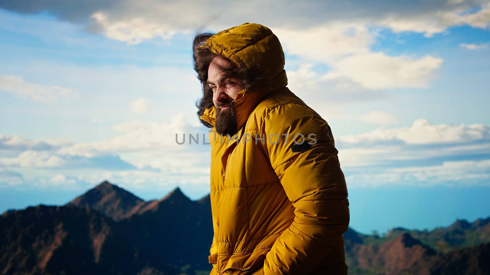 Young traveler struggling with cold winds on top of the mountain, feeling proud of his trekking activity. Adventure seeker with ambition successfully climbing the mountain range. Camera A.