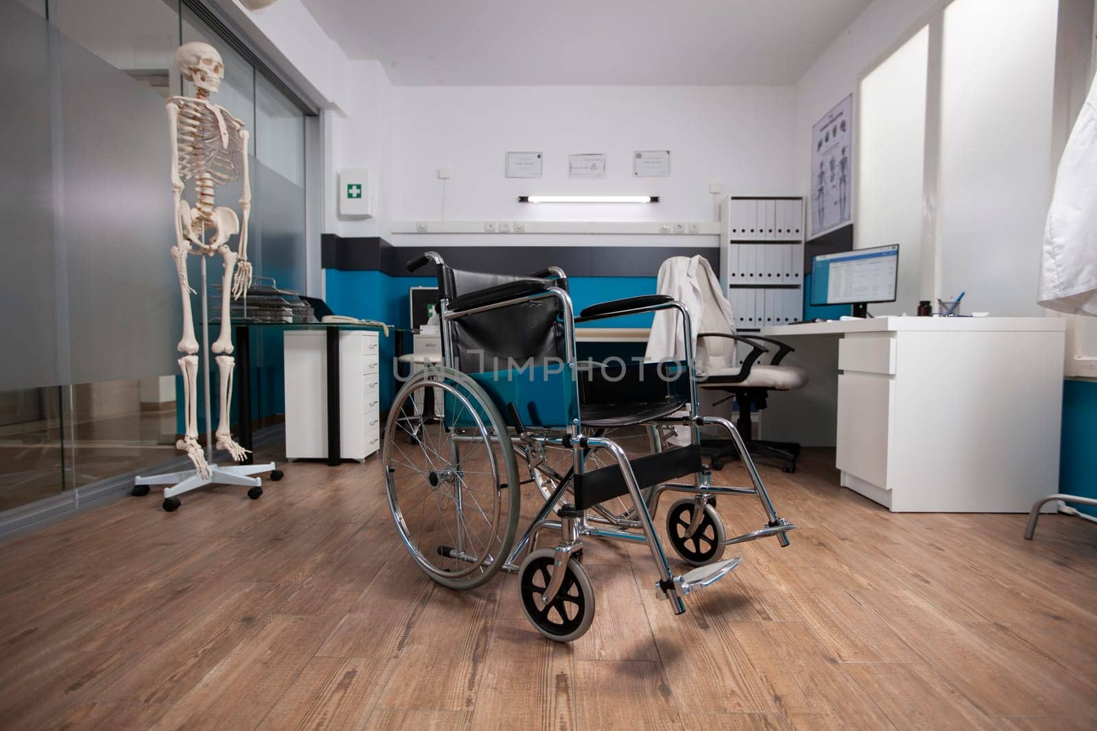 Vacant examination room showcasing a medical wheelchair and anatomical skeletal model, ready for patient treatment. Modern technology and healthcare tools are neatly organized in empty doctors office.