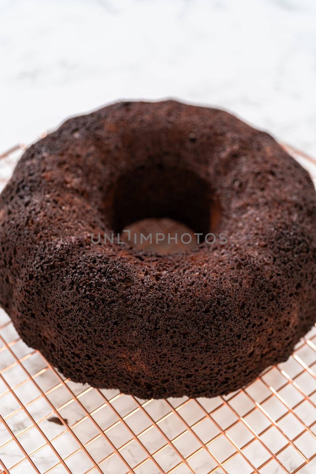 With precision, the Chocolate Bundt Cake is carefully removed from the pan - placed onto a round cooling rack, preparing it for a flawless presentation and delightful indulgence.
