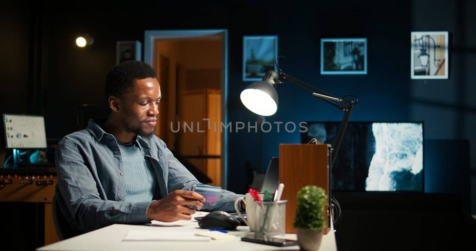 Casual guy purchasing products on electronic app with his credit card, ordering apparel on internet during promotional season. Black man feels satisfied as he enters payment information. Camera A.