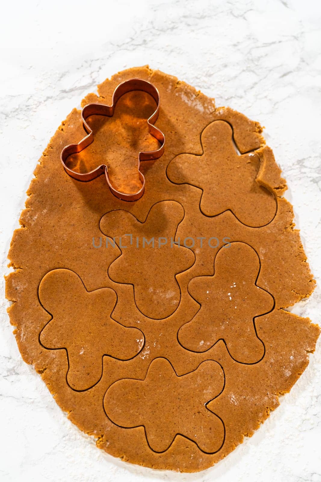 Close-up of a cookie cutter pressing into gingerbread dough on a floured surface.