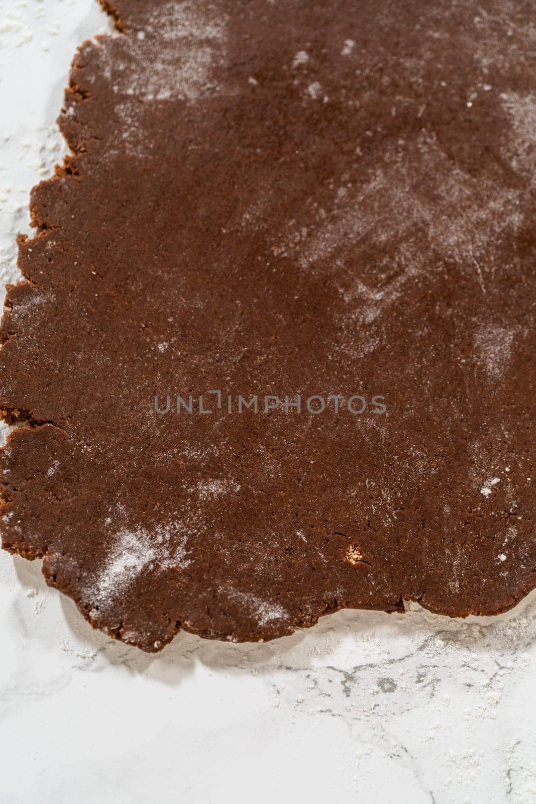 Overhead view of chocolate cookie dough partially rolled out on a floured marble surface, prepped for cookie cutting.