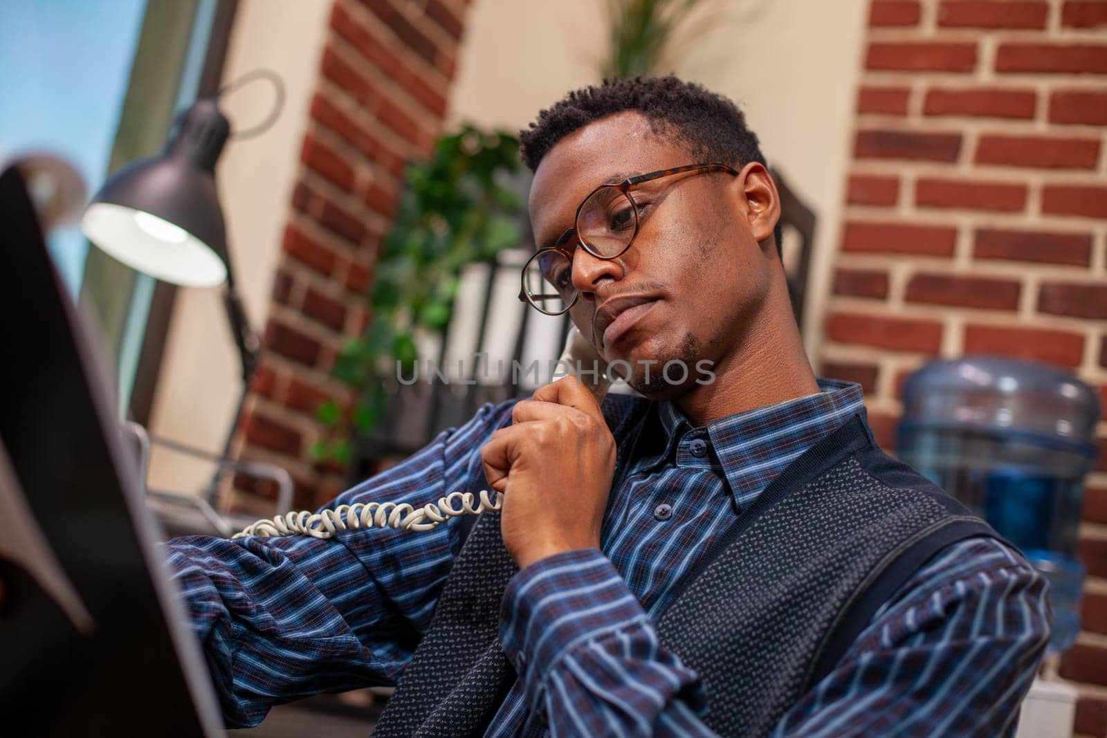 Closeup of african american marketer looking at clipboard with analytics charts, discussing turnover results with client on phone. Businessman holding landline to ear and reviewing research documents.