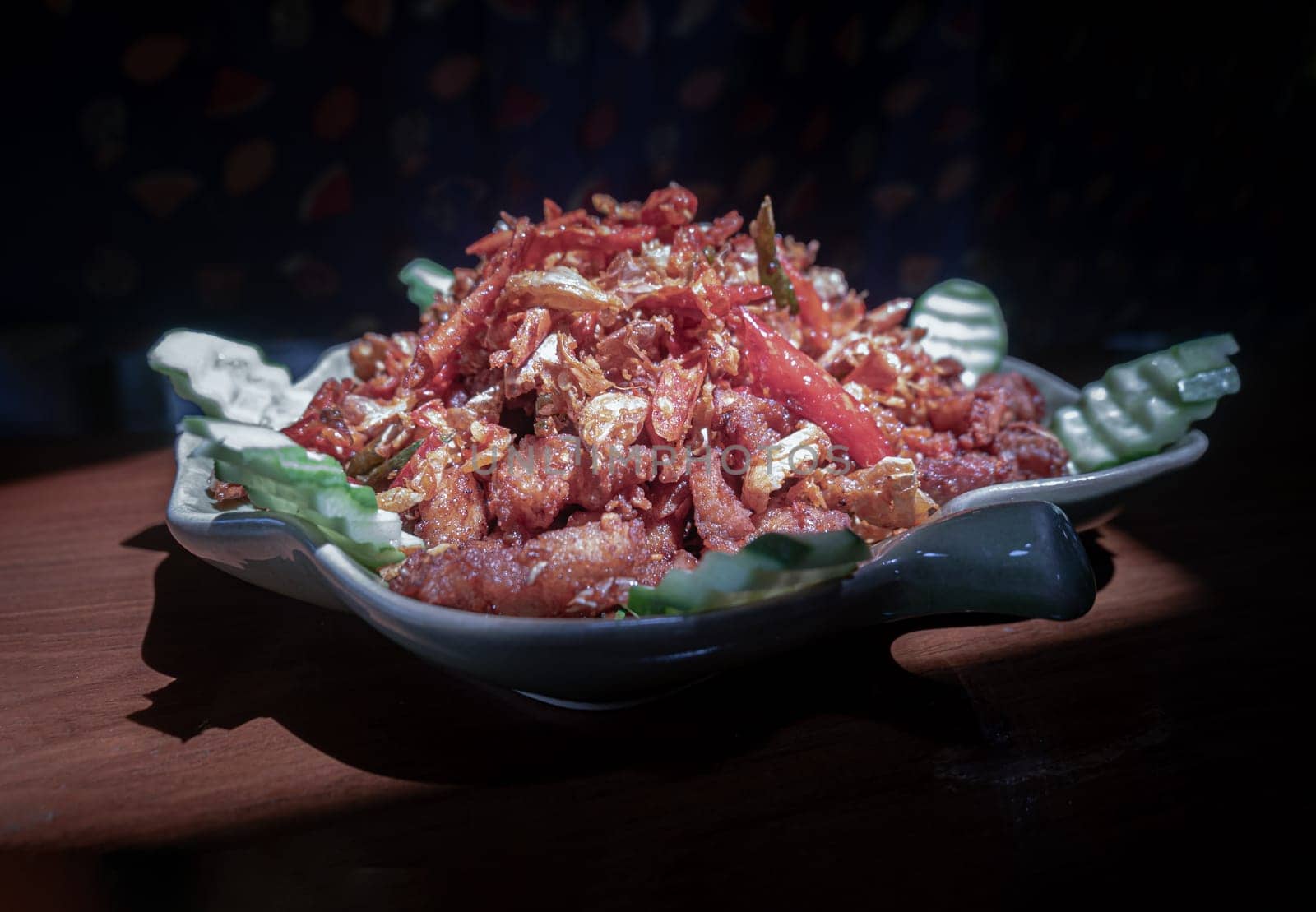 Stir-fried Pork belly with Salt chilli and sprinkled with Fried garlic and Fried red chilies on Ceramic plate. use it as your Wallpaper, Poster and Space for text, Selective focus.