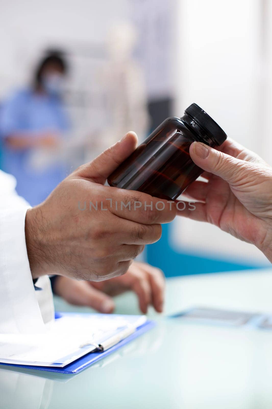 Closeup of hands of caucasian people holding container of prescribed medicine at desk in medical office. Physician handing over health supplements to patient during clinic appointment.