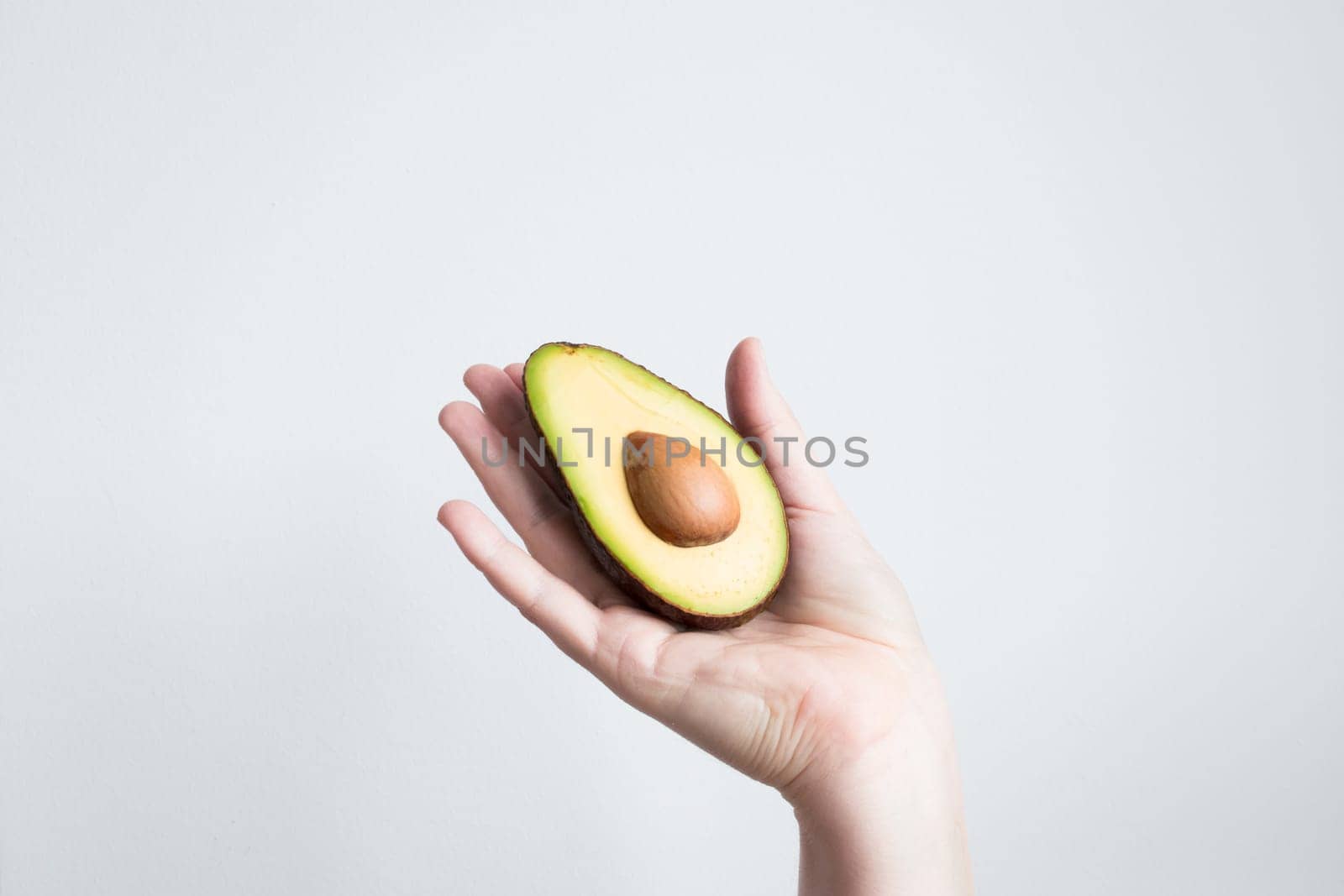 Hand holding half avocado against white background.