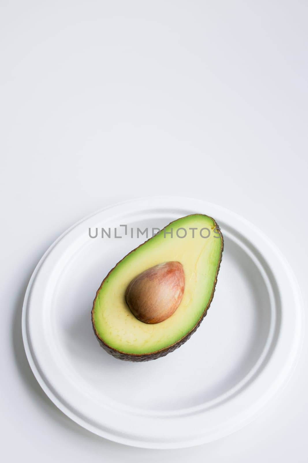 Halved ripe avocado on white plate against minimalistic background.
