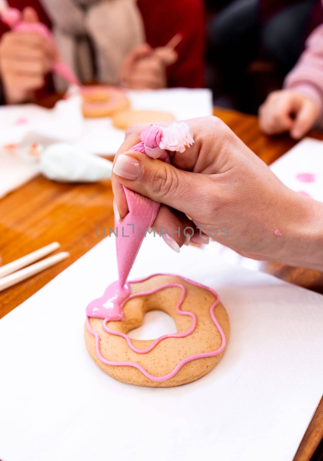 Female decorating pink icing cookie with piping bag at baking class.