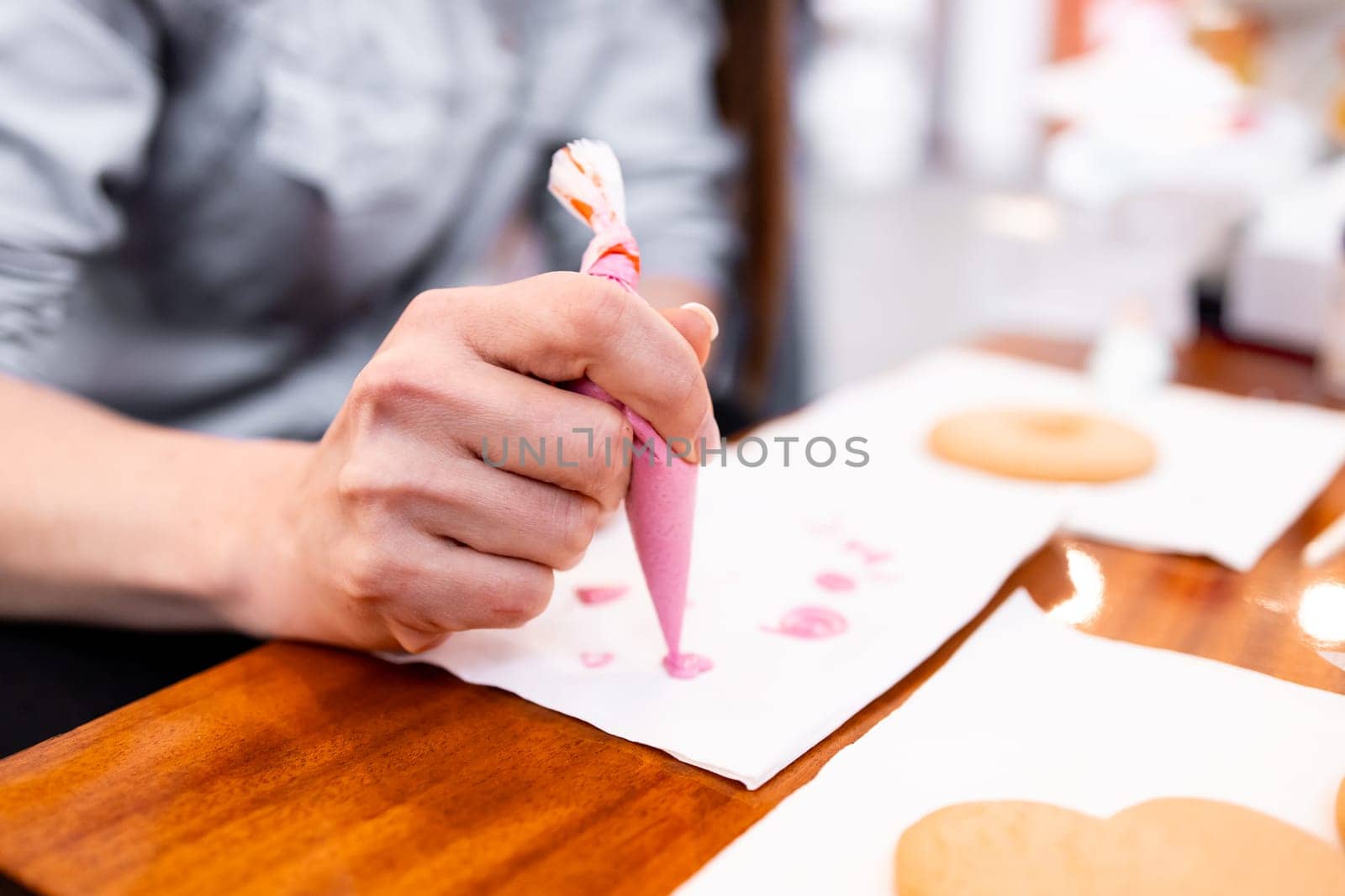 Adult female decorating cookies with pink icing using a piping bag in a kitchen setting.