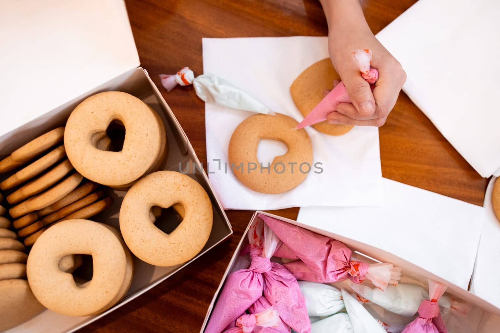 Decorating heart shaped cookies with icing by hand on wooden table.