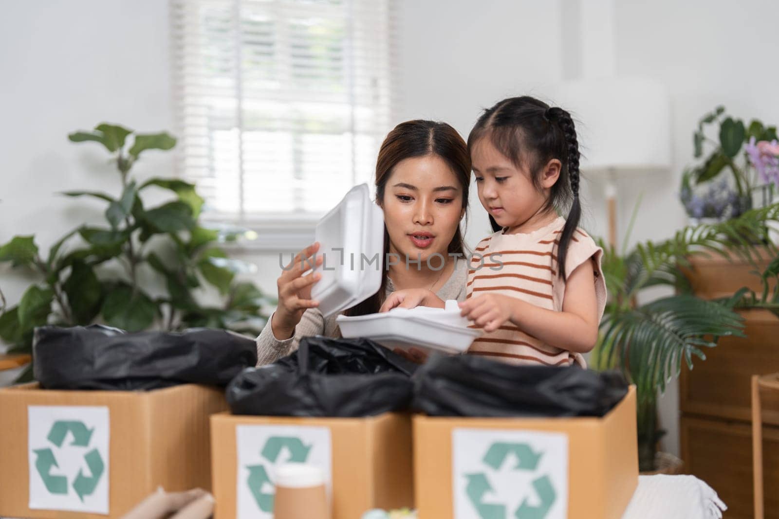 While sorting recyclable containers, a mother teaches her daughter about sustainability, fostering a sense of responsibility and care for the planet.