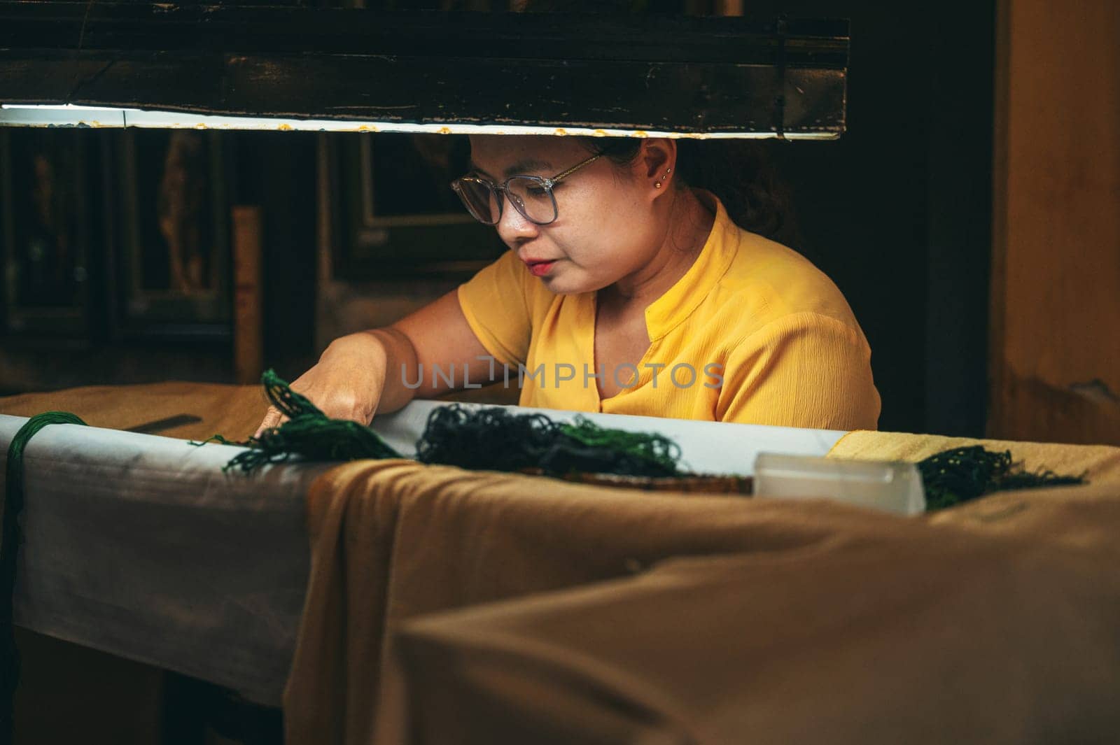 A Vietnamese female embroiderer embroiders a silk painting in a workshop in the old town in Hoi An city in Asia. Hoi An, Vietnam - December 1, 2024