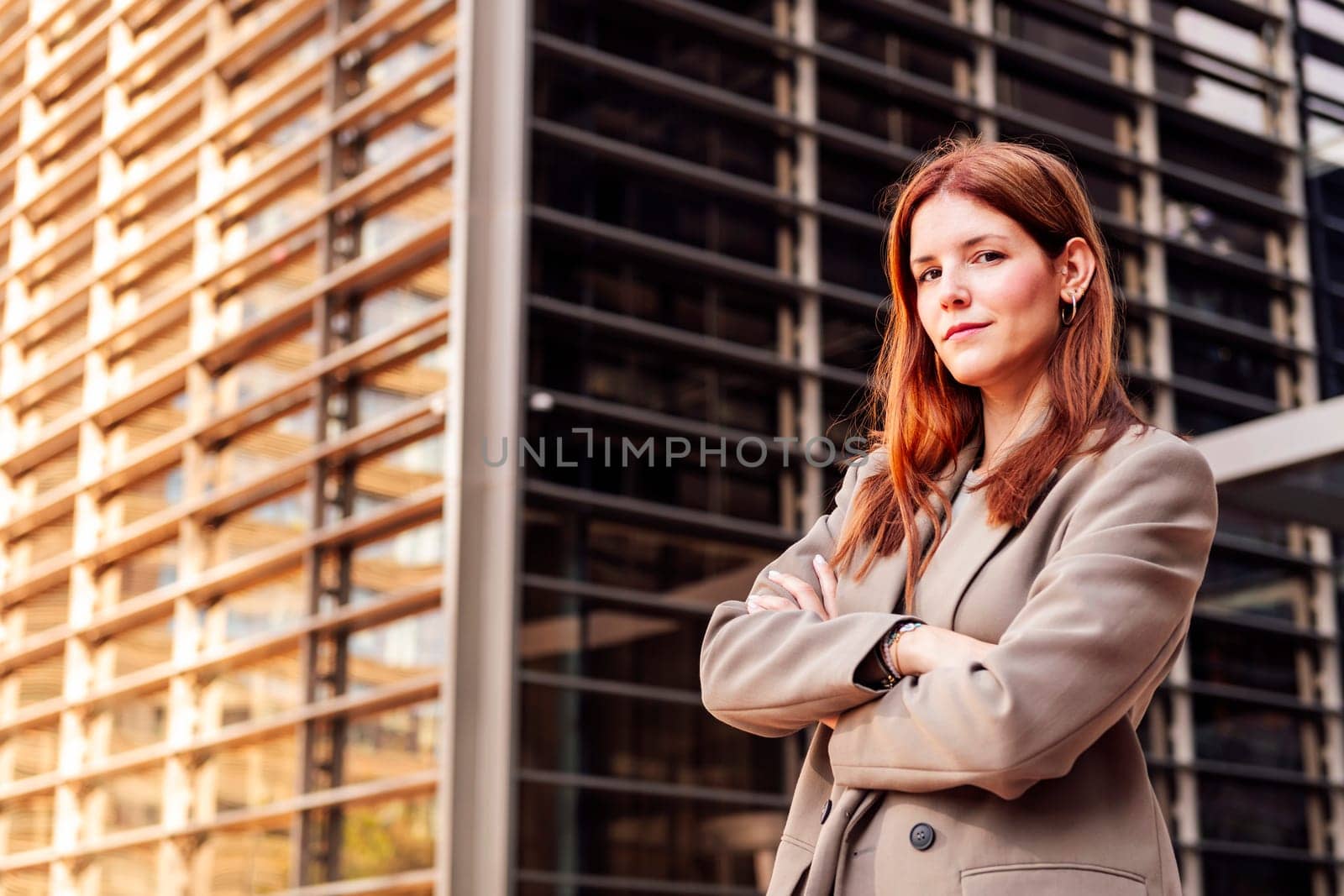 young adult woman in suit jacket standing looking at camera with arms crossed in front of an office building, concept of entrepreneur and business, copyspace for text