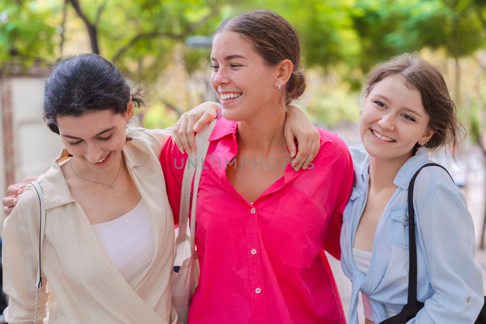 three gossipy teenagers chatting outdoors. A group of Caucasian friends chatting and communicating. Young adult students smiling and walking together at a social gathering.