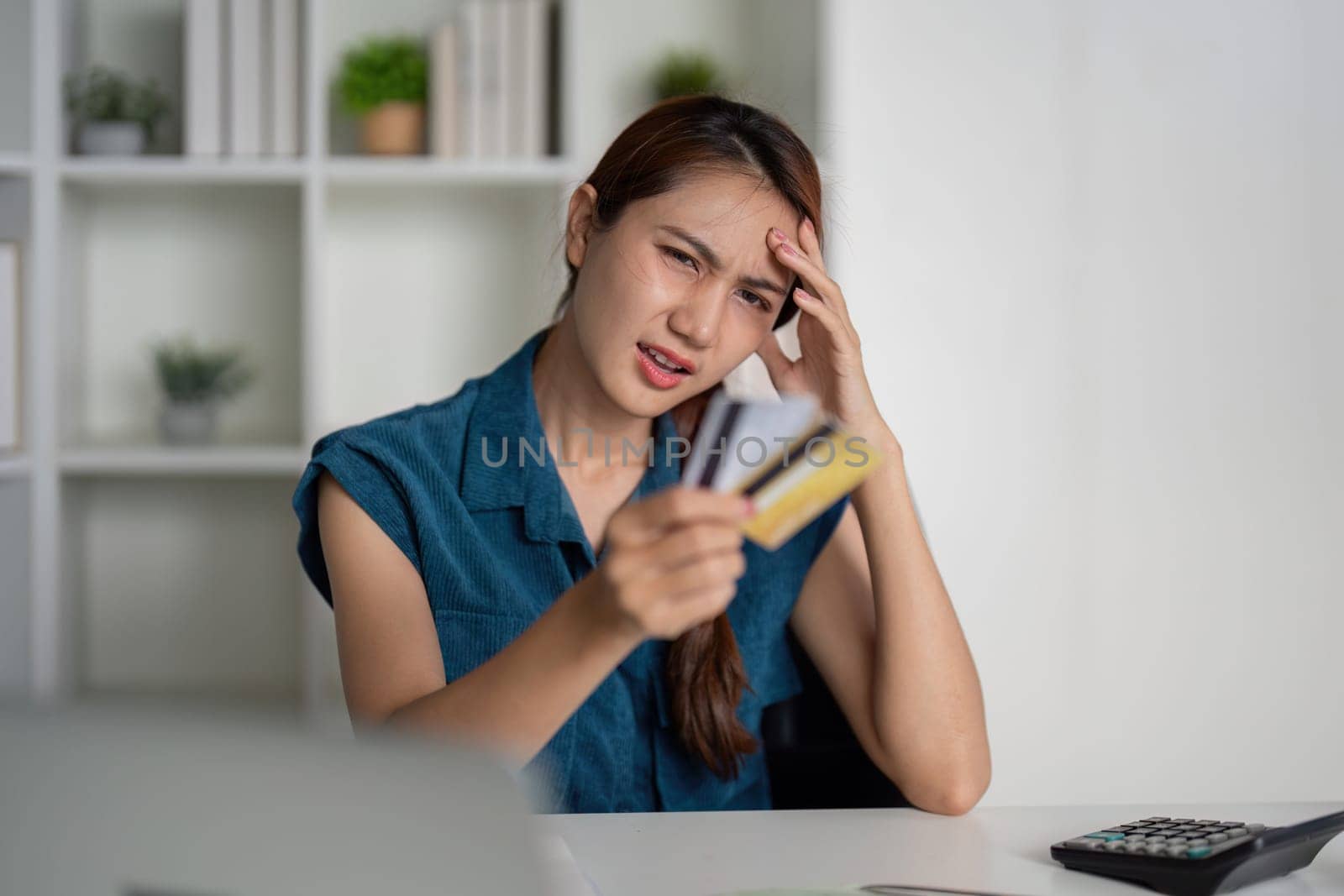 A woman looks overwhelmed as she examines her credit cards, feeling the weight of financial decisions. Her expression reflects concern over her spending habits.
