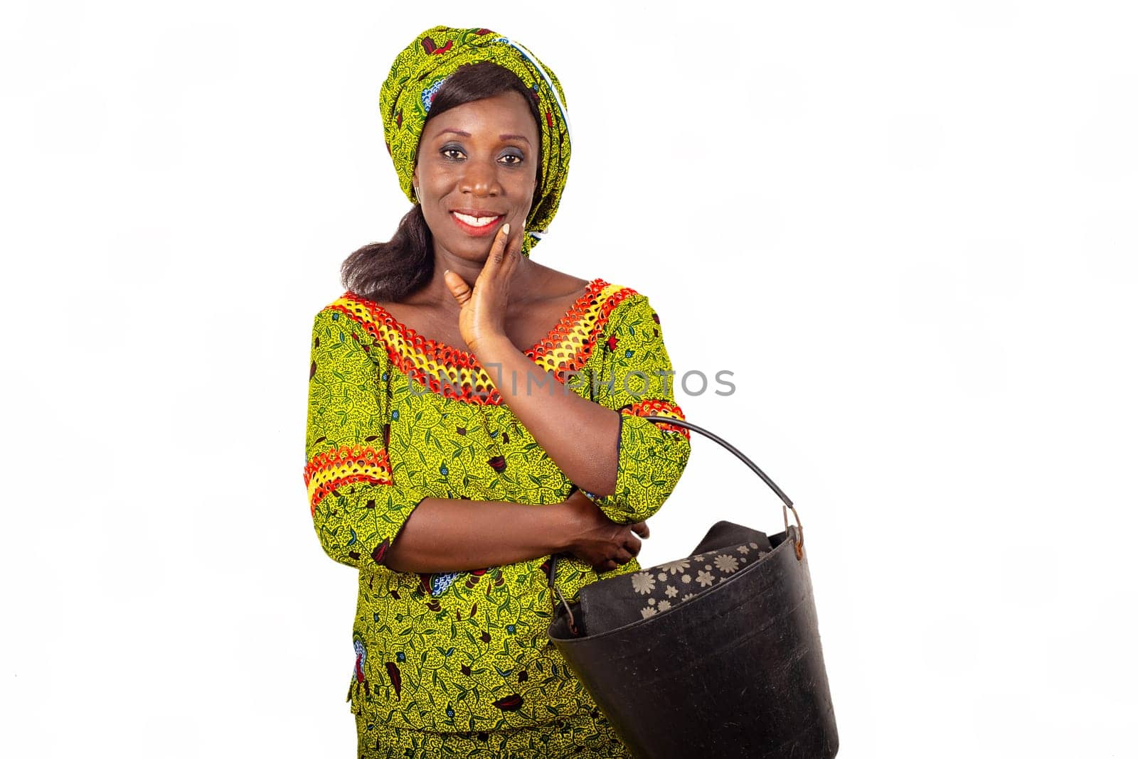 beautiful african adult woman dressed in green loincloth, puts on arm a beautiful black bucket smiling