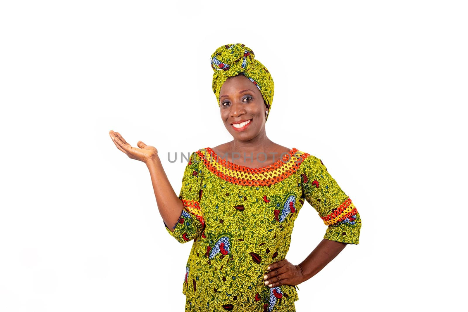 Beautiful african adult woman wearing a loincloth and a green scarf on her head with her arm crossed and her hand raised smiling