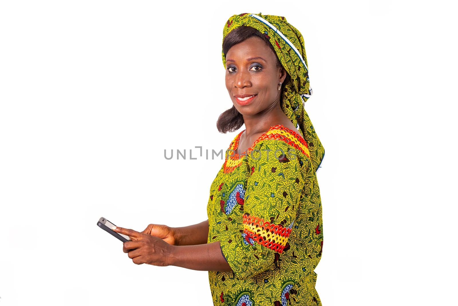 beautiful african adult woman wearing a green loincloth stuck with a mobile phone looking at one side smiling