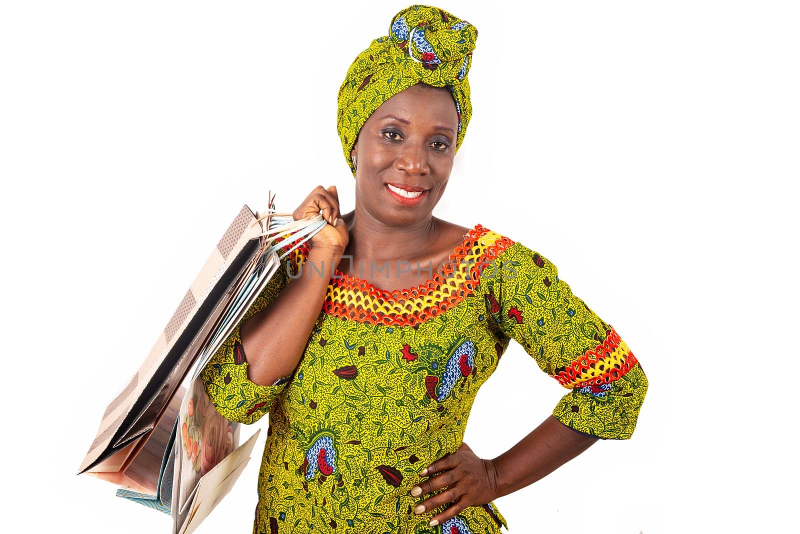 beautiful african adult woman wearing a loincloth and a green scarf is smiling and happy with shopping bags in hand raised and arms crossed