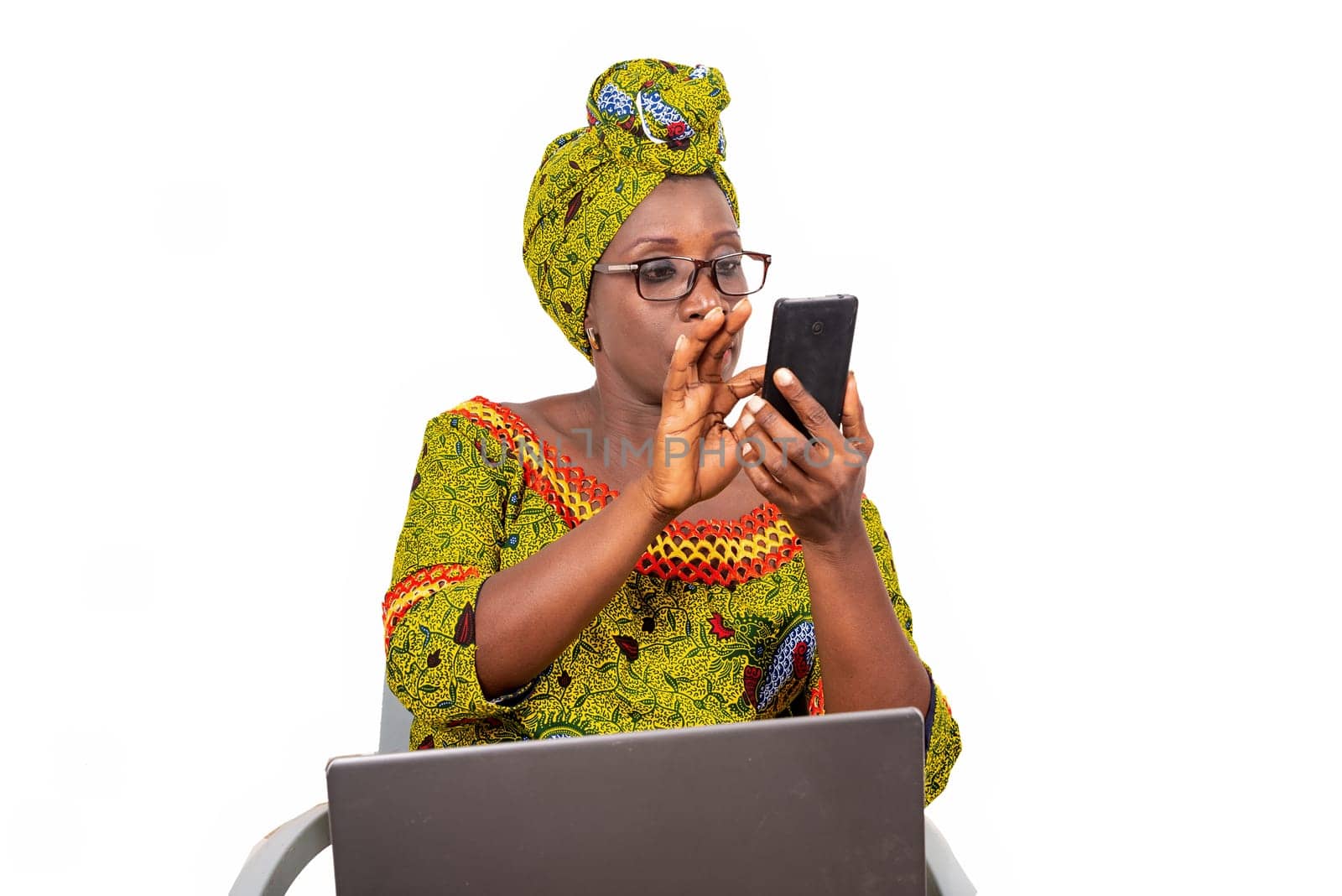 beautiful mature woman in glasses isolated on white background looking at mobile phone with laptop on her thighs.