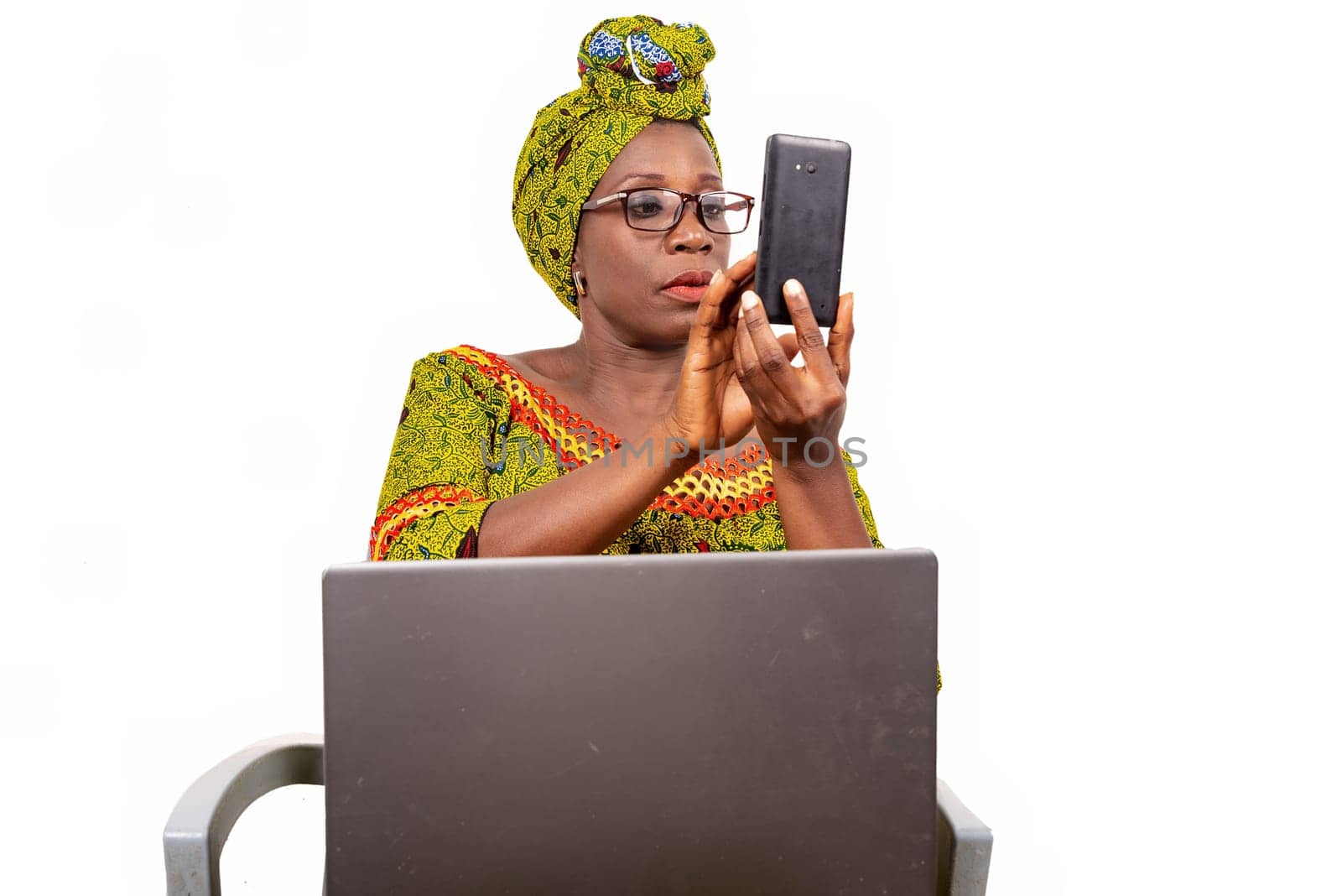 beautiful mature woman in glasses isolated on white background looking at mobile phone with laptop on her thighs.