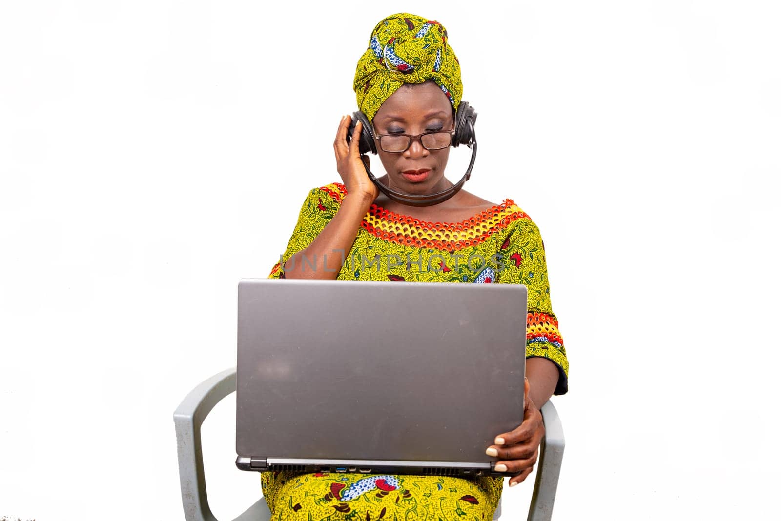 beautiful mature woman in eyeglasses isolated on white background communicating with laptop using headphones.