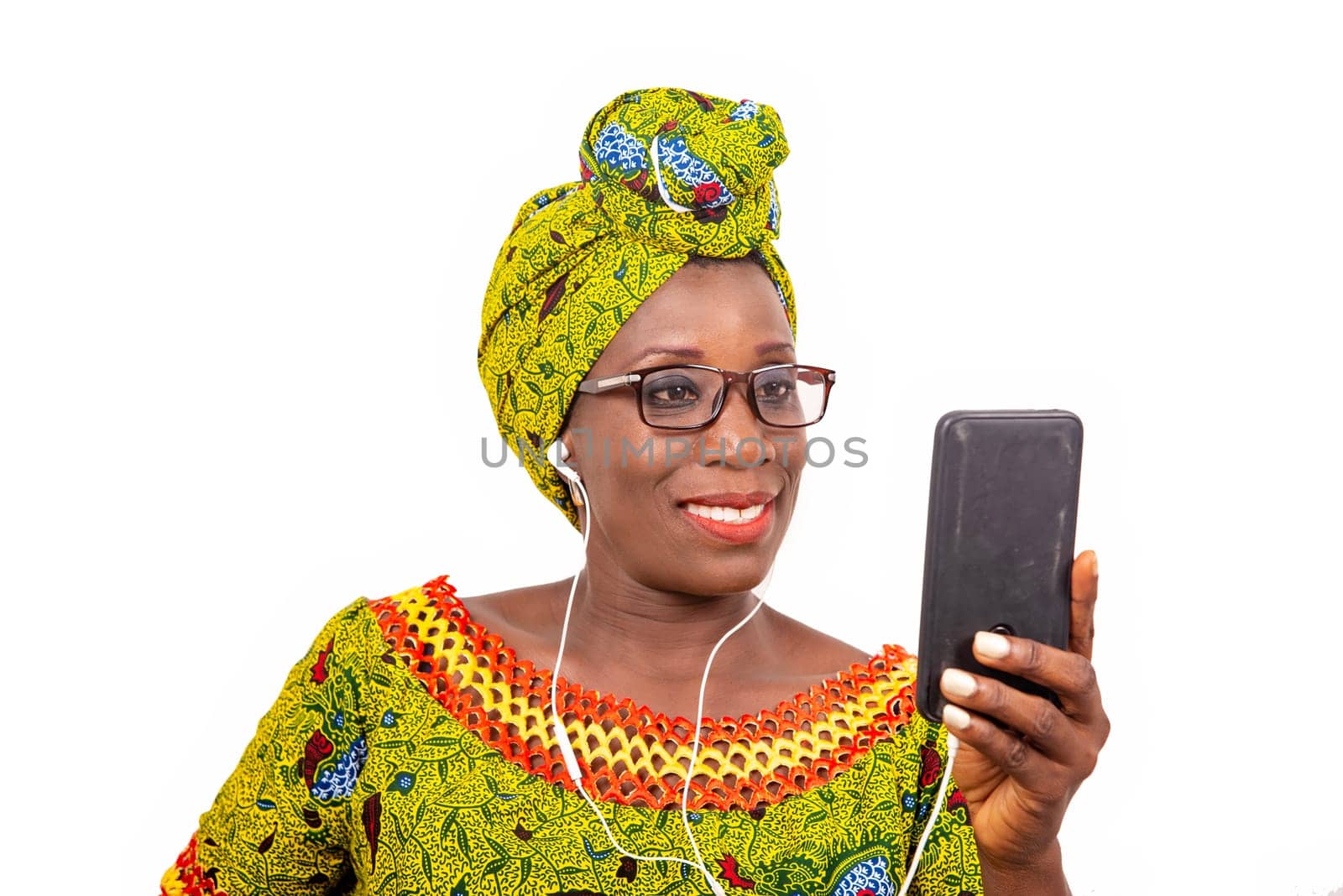 beautiful african adult woman dressed in loincloth and green scarf with glasses, takes pleasure communicating with headphones, in his mobile while smiling