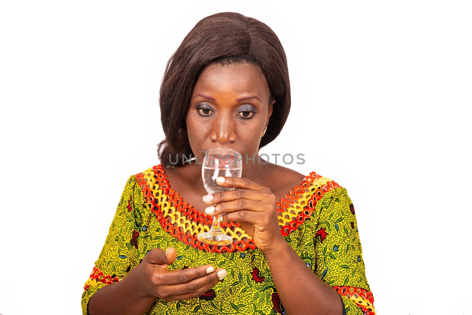 beautiful african adult woman wearing a green loincloth with long black hair, is drinking mineral water in a glass