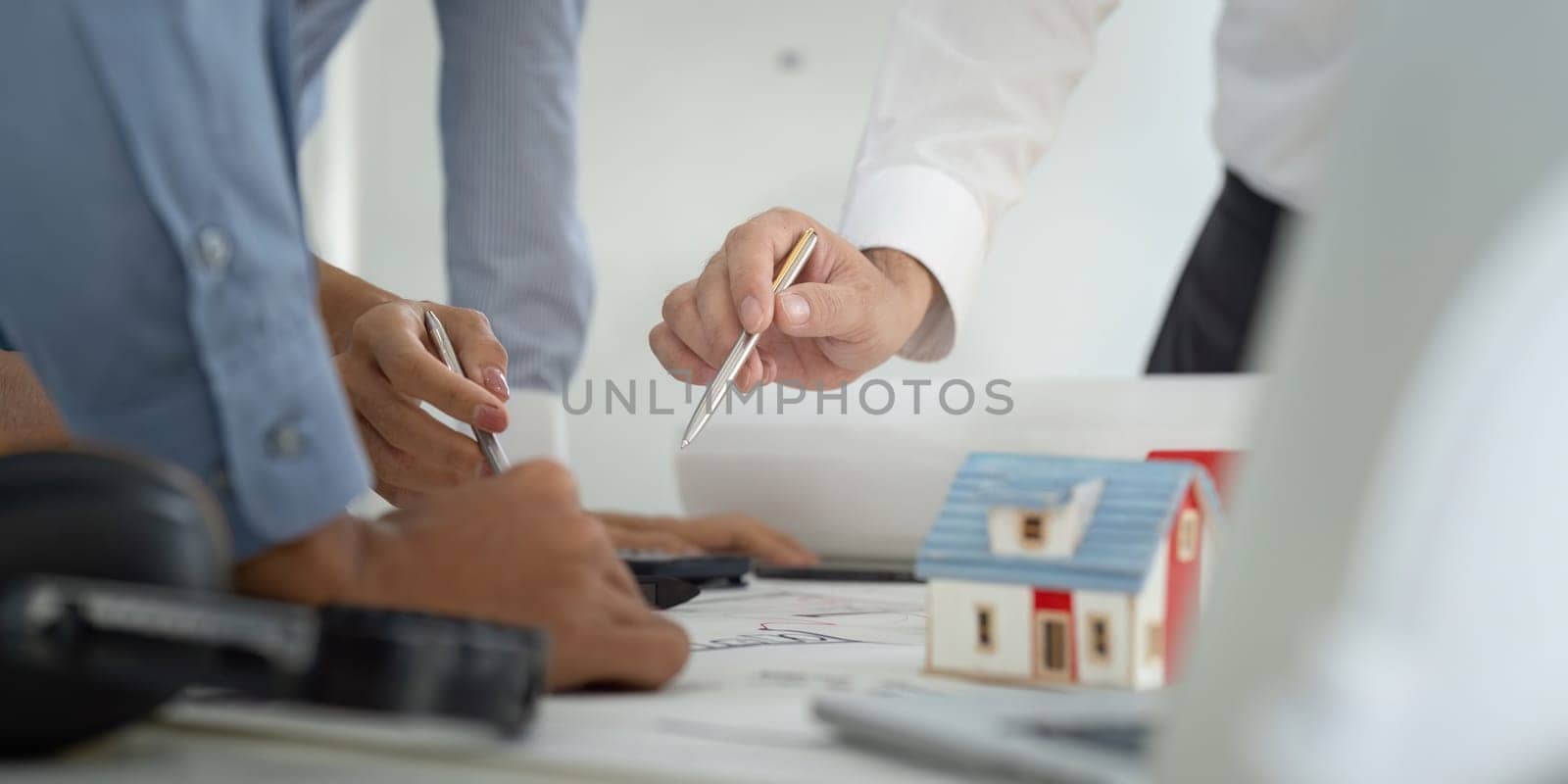 A focused team discusses design strategies over construction plans, utilizing tools and a mini house model to visualize the project.