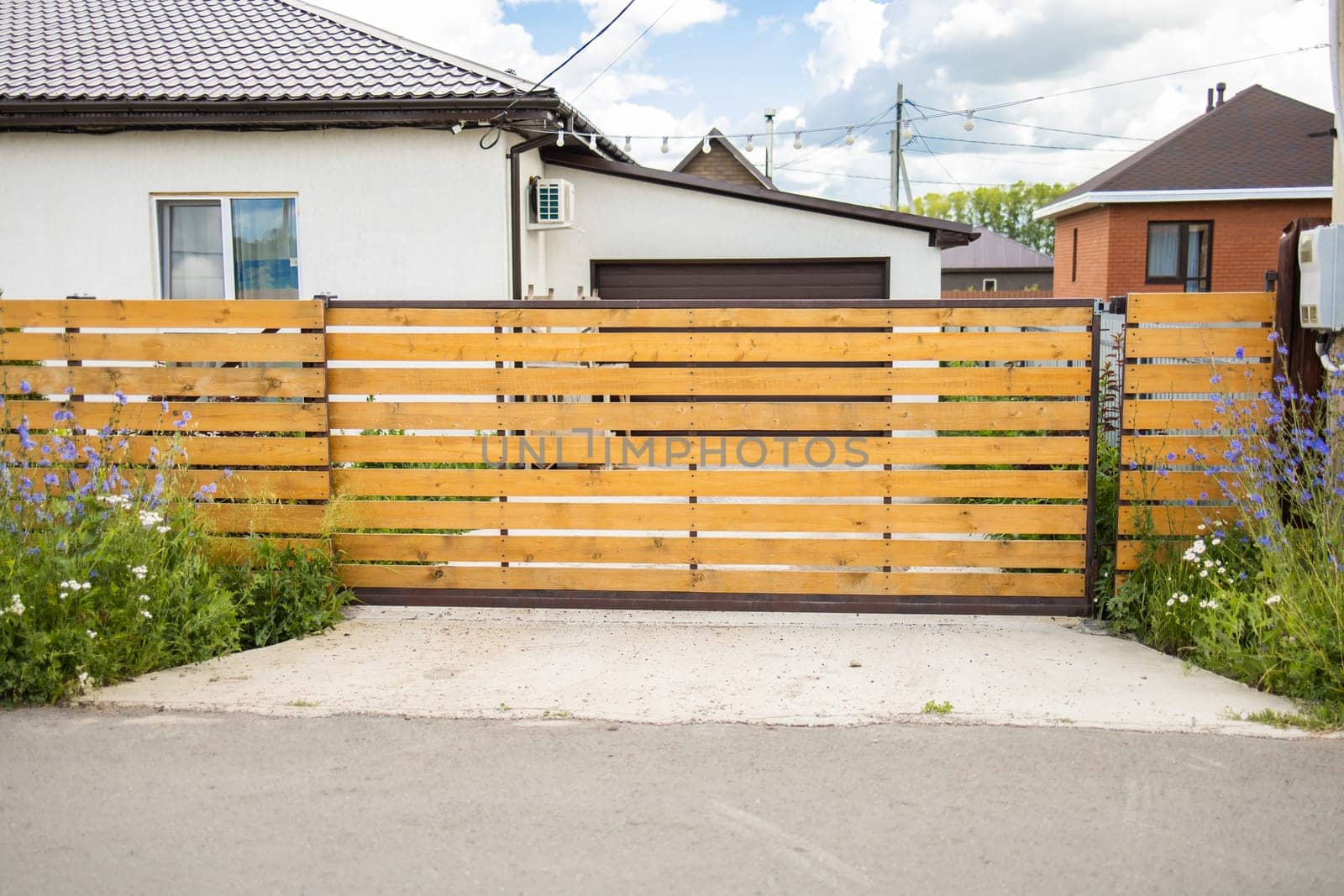 Wooden fence with closed gate and flowers in front of house. Closed access, natural border, and welcoming suburban entrance design.