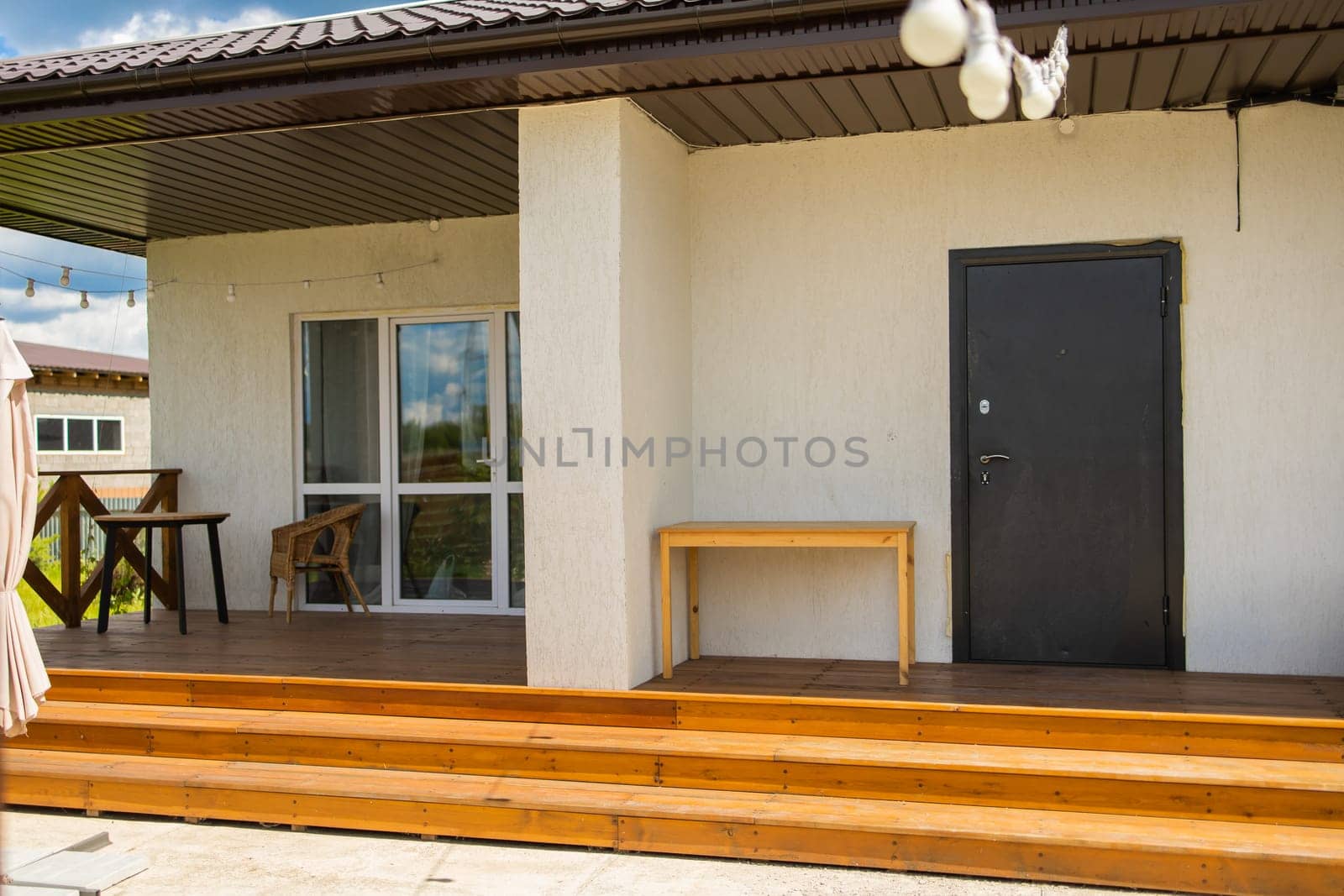 Wooden steps lead to porch with black door and wicker chair. Simple architectural structure and functional outdoor space usage