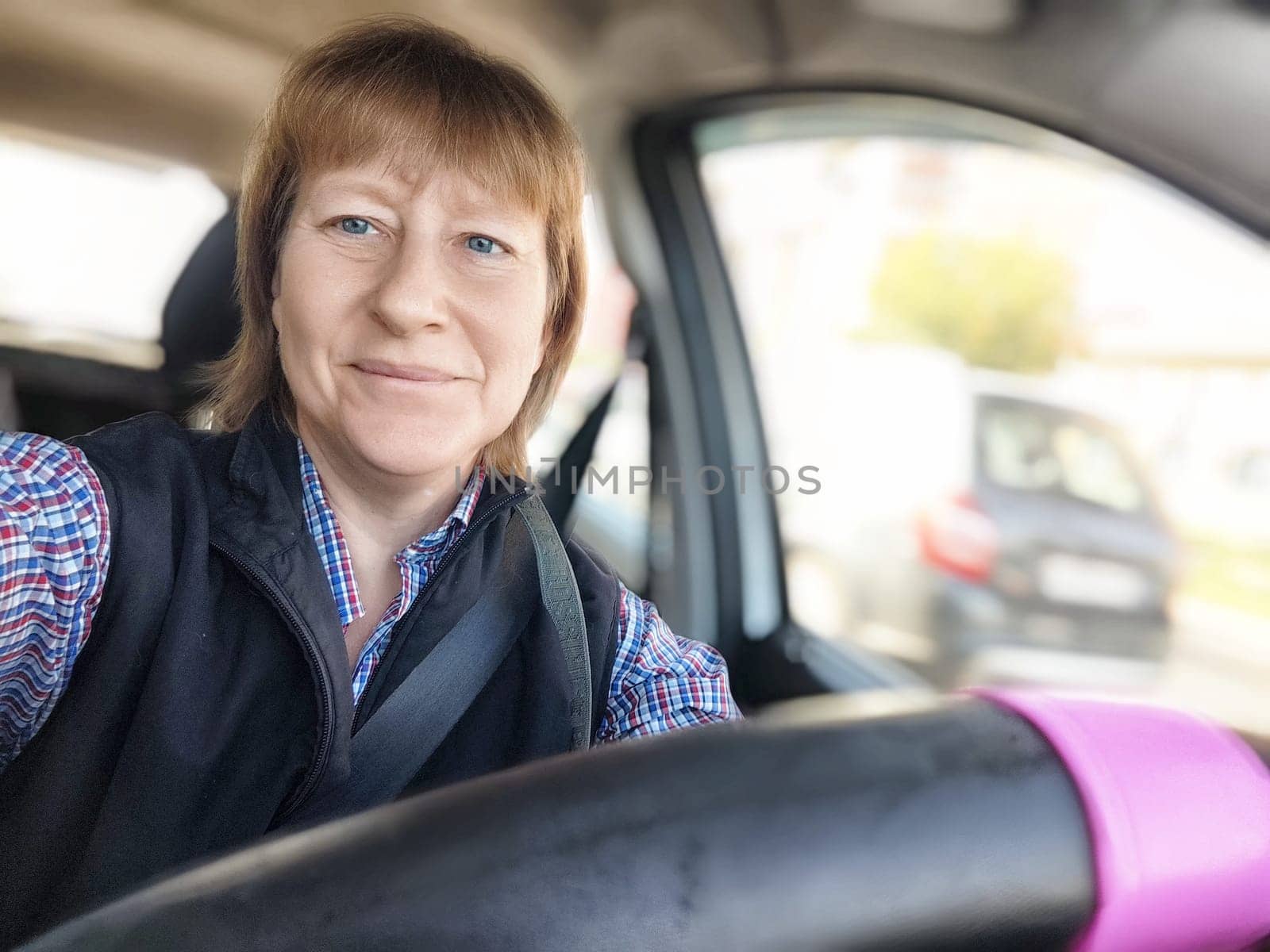 A middle-aged woman with blonde hair smiles while driving, capturing a moment of her travel journey.
