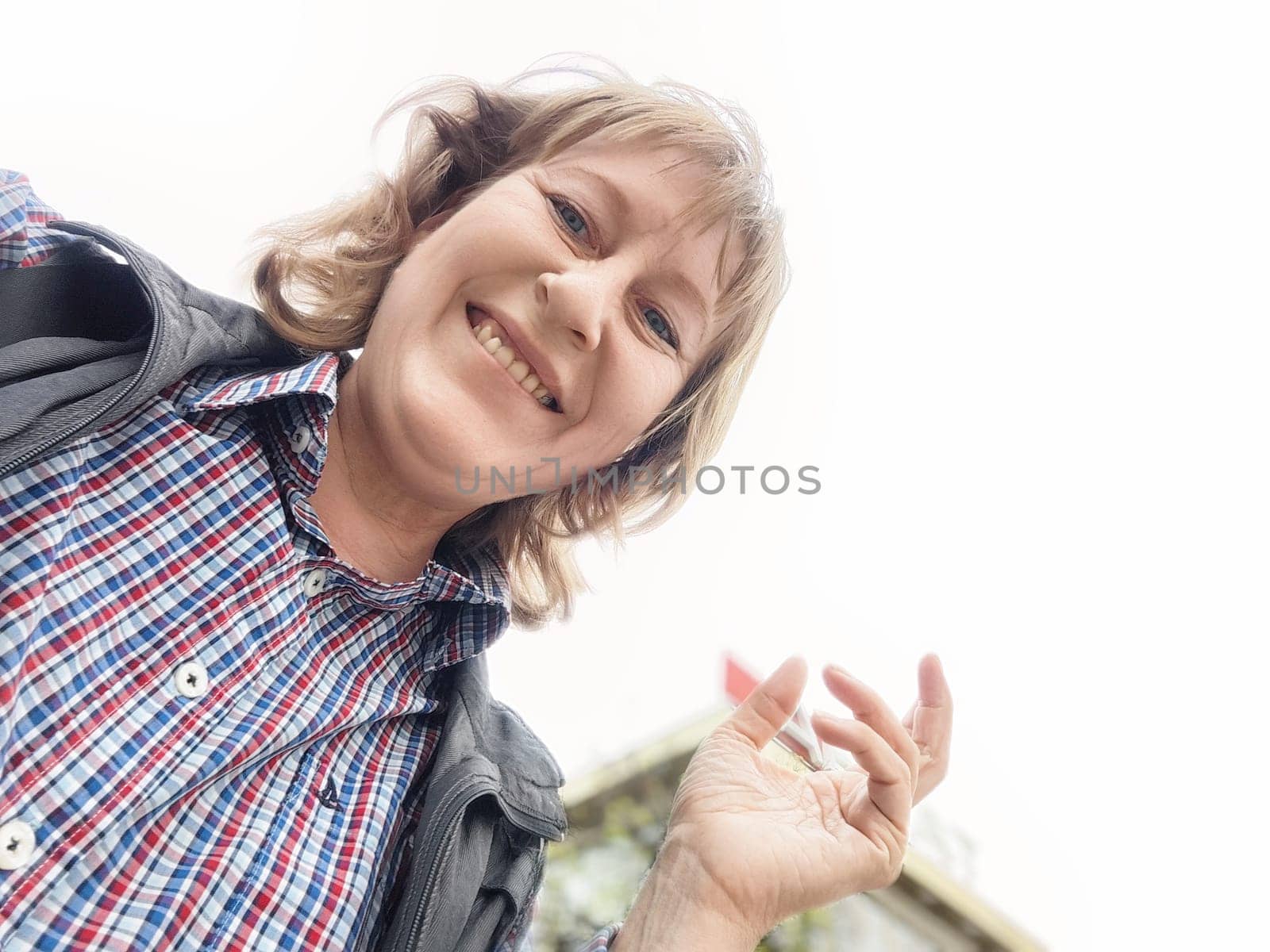 This middle-aged blonde woman enjoys her travel trip while taking a selfie, smiling brightly in a casual setting.