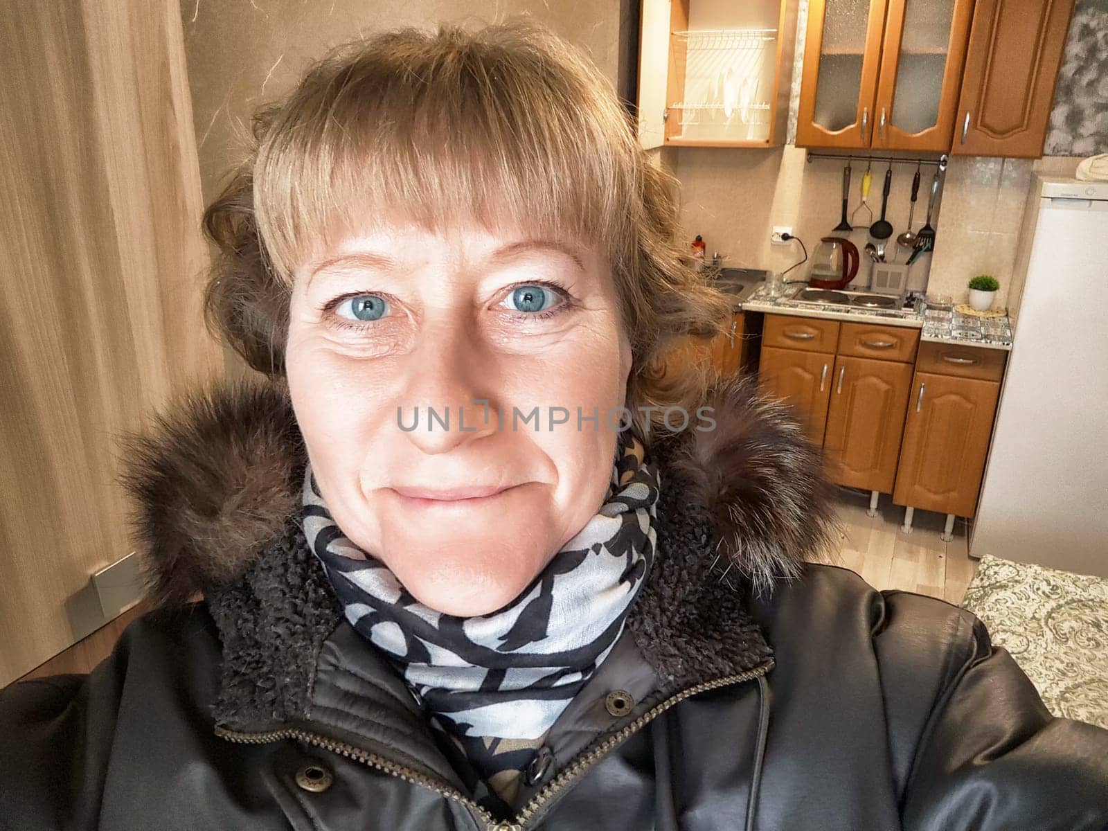 A woman with bright eyes smiles for a selfie while indoors in a nicely arranged kitchen during winter.