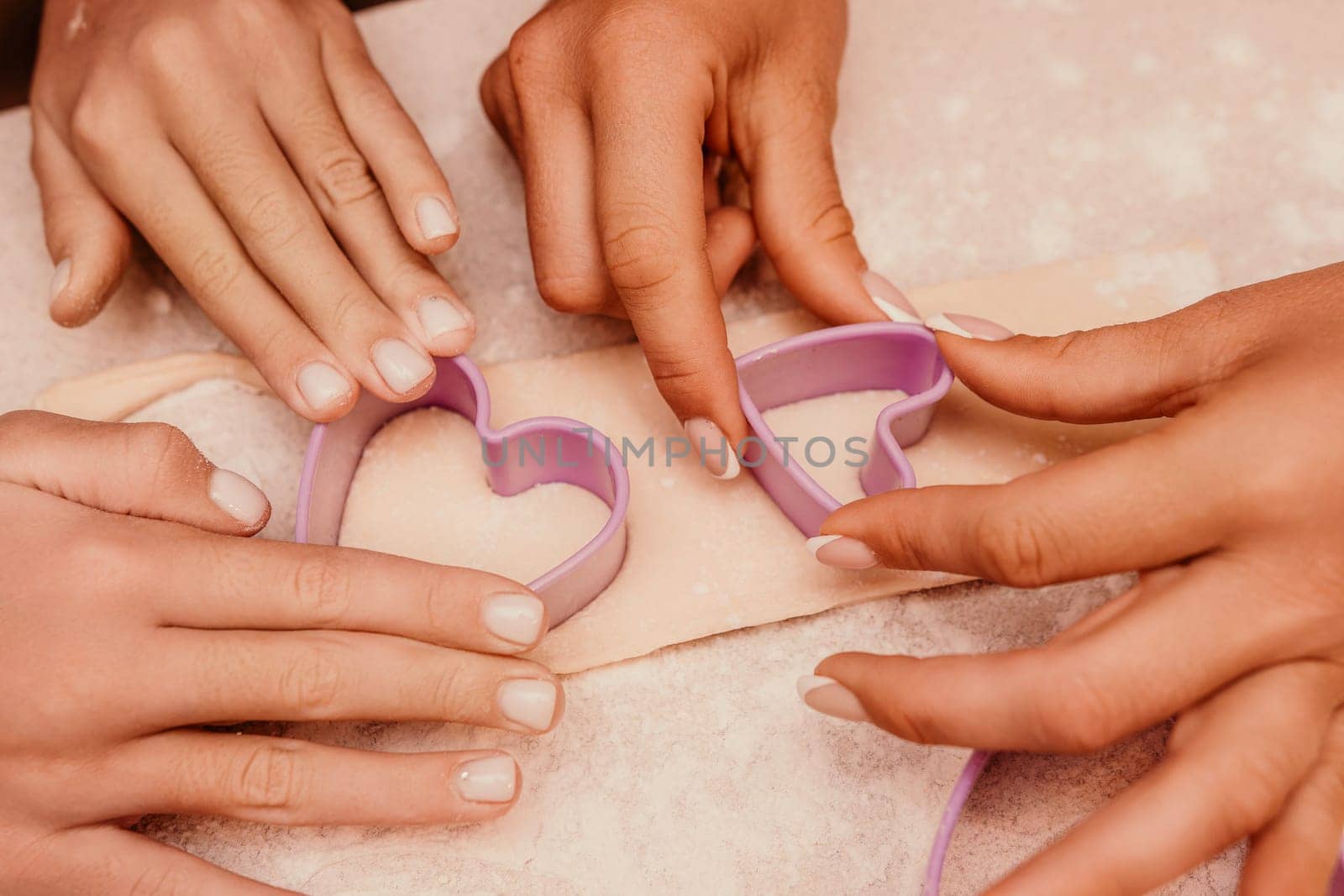 Four hands use a heart-shaped cookie cutter to cut out shapes from dough.