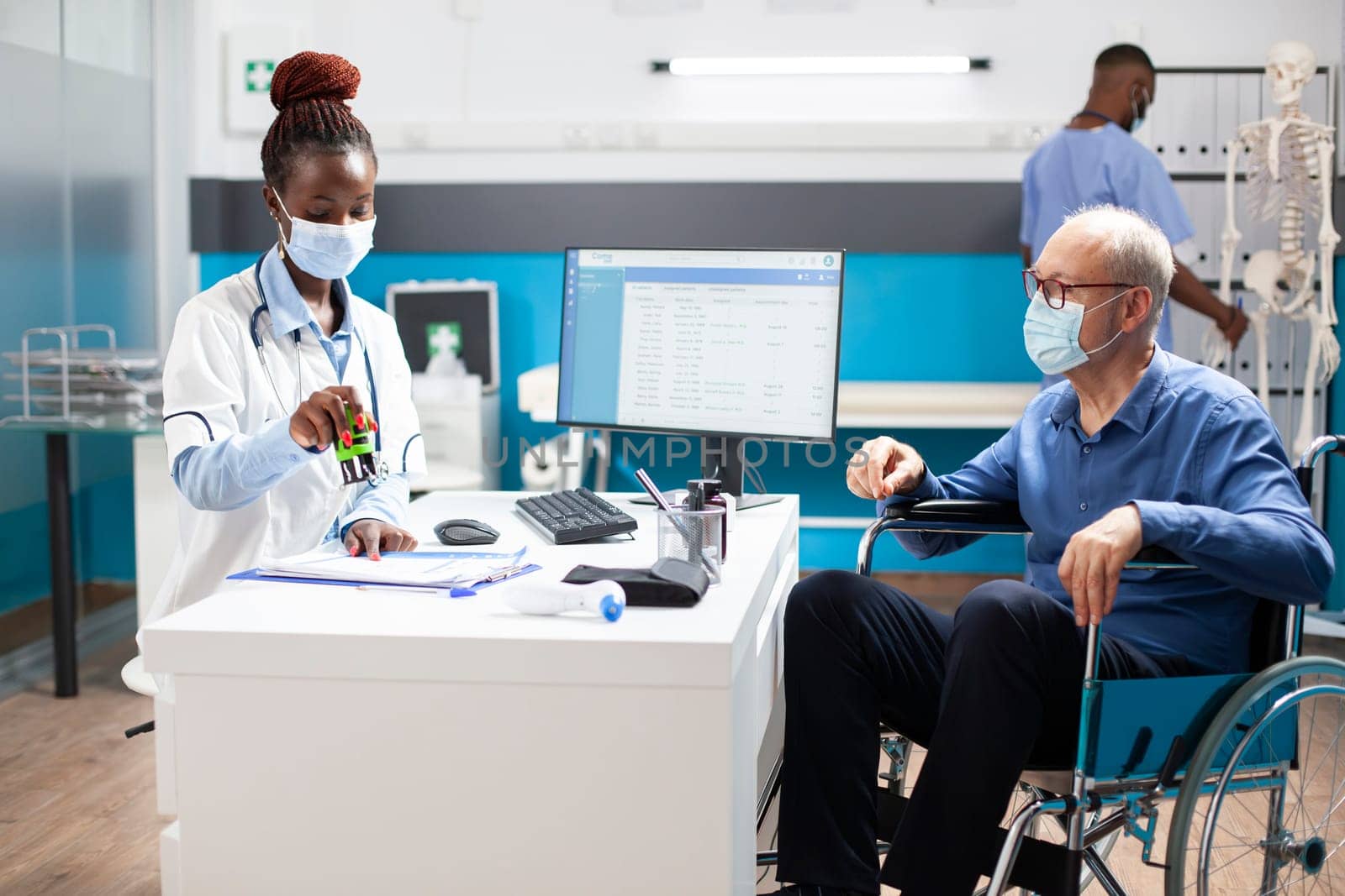 Female healthcare provider stamps paperwork on clipboard with elderly man listening closely during consultation. Caucasian male wheelchair user awaiting his medical prescription from female doctor.