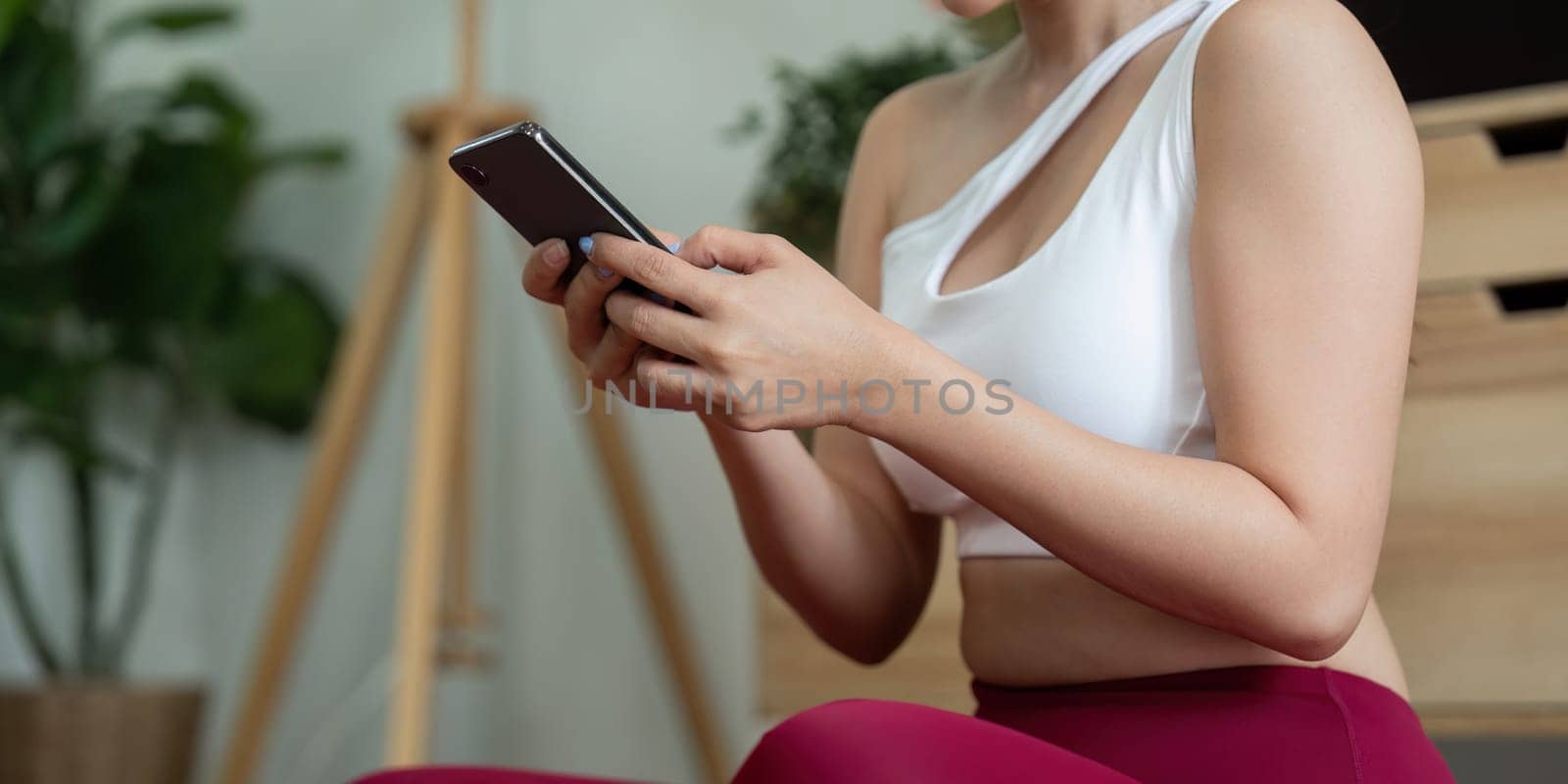 A fitness enthusiast practices yoga indoors, balancing technology and wellness. She focuses on her phone to follow along with a guided yoga session.