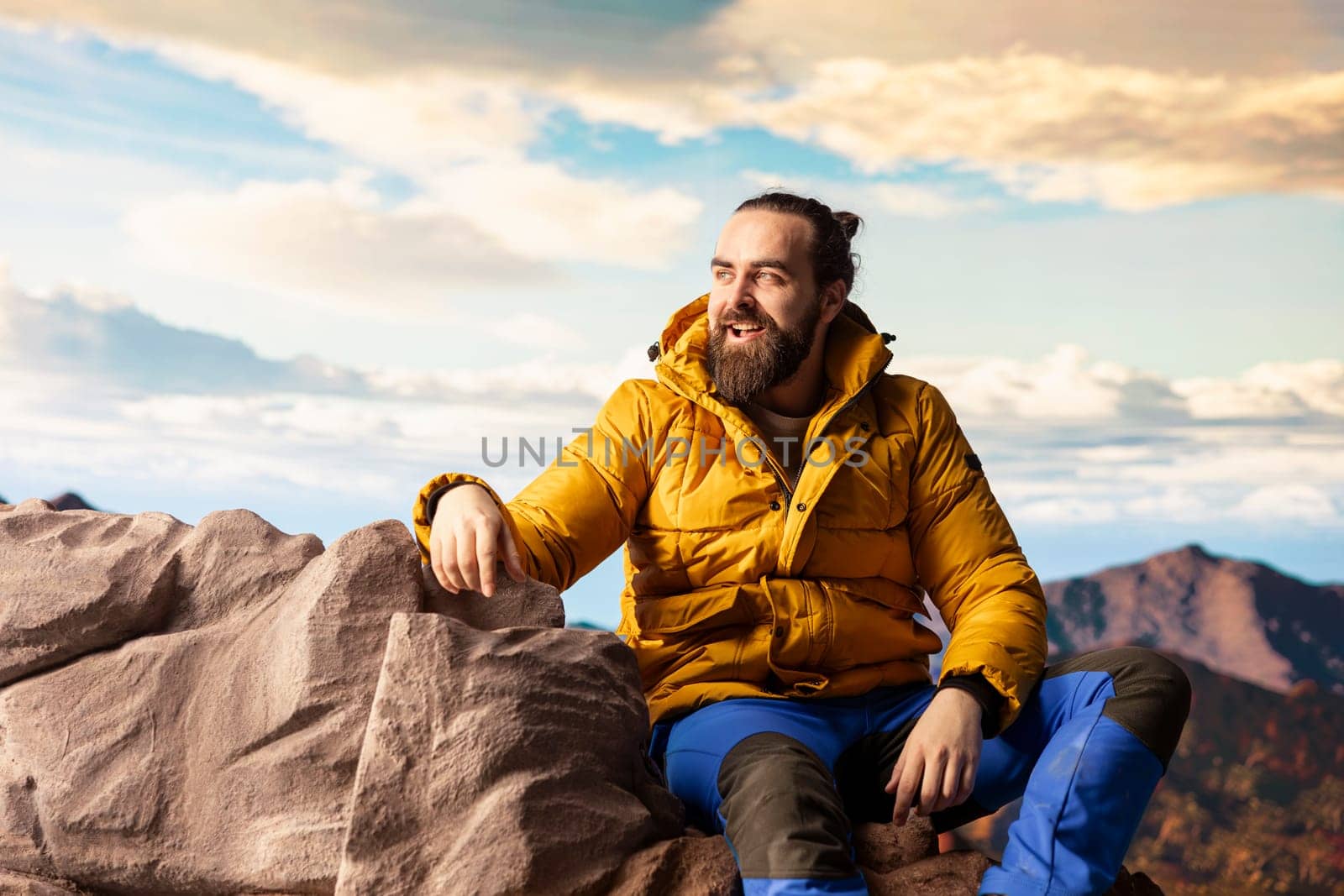 Traveler stands alone at the edge of a towering mountain range, gazing at the clouds and stunning panoramic scenery. Pleased hiker showcasing personal growth and perseverance.