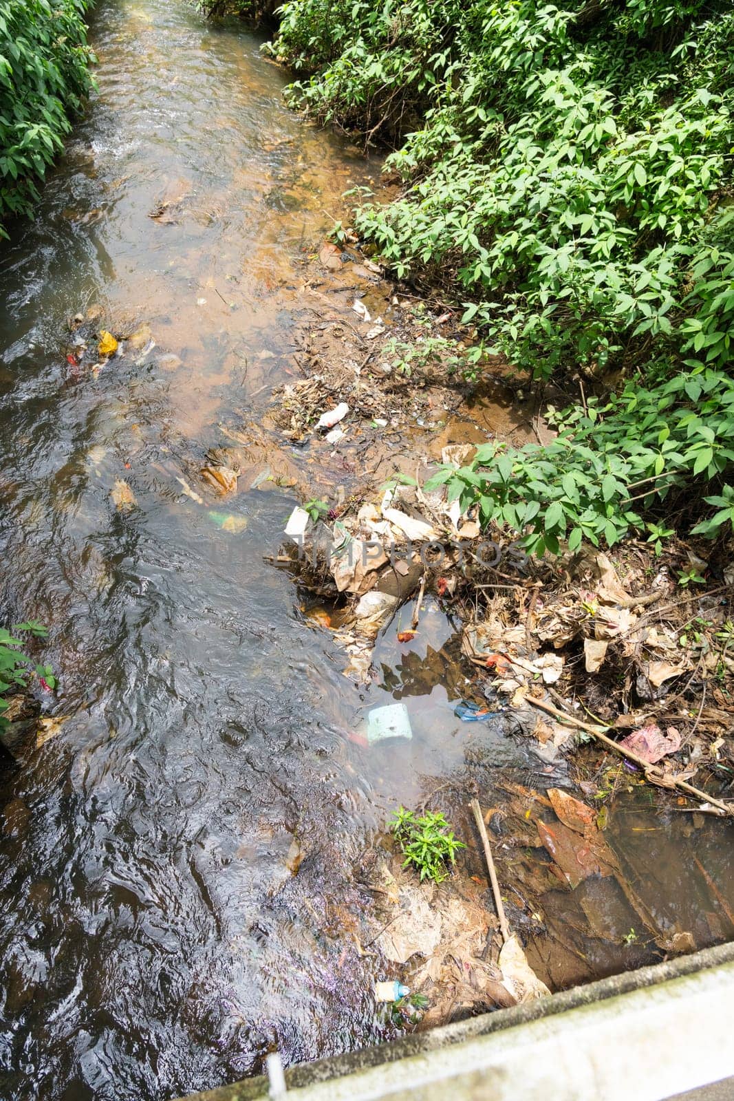 Environmentally damaging trash carelessly discarded in city creek in Asian city.