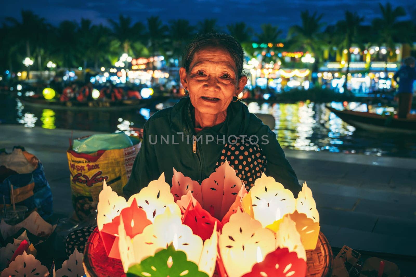 Old elderly Vietnamese woman sells paper lanterns for a festive festival by river in old town in Hoi An city in Asia. Hoi An, Vietnam - December 1, 2024