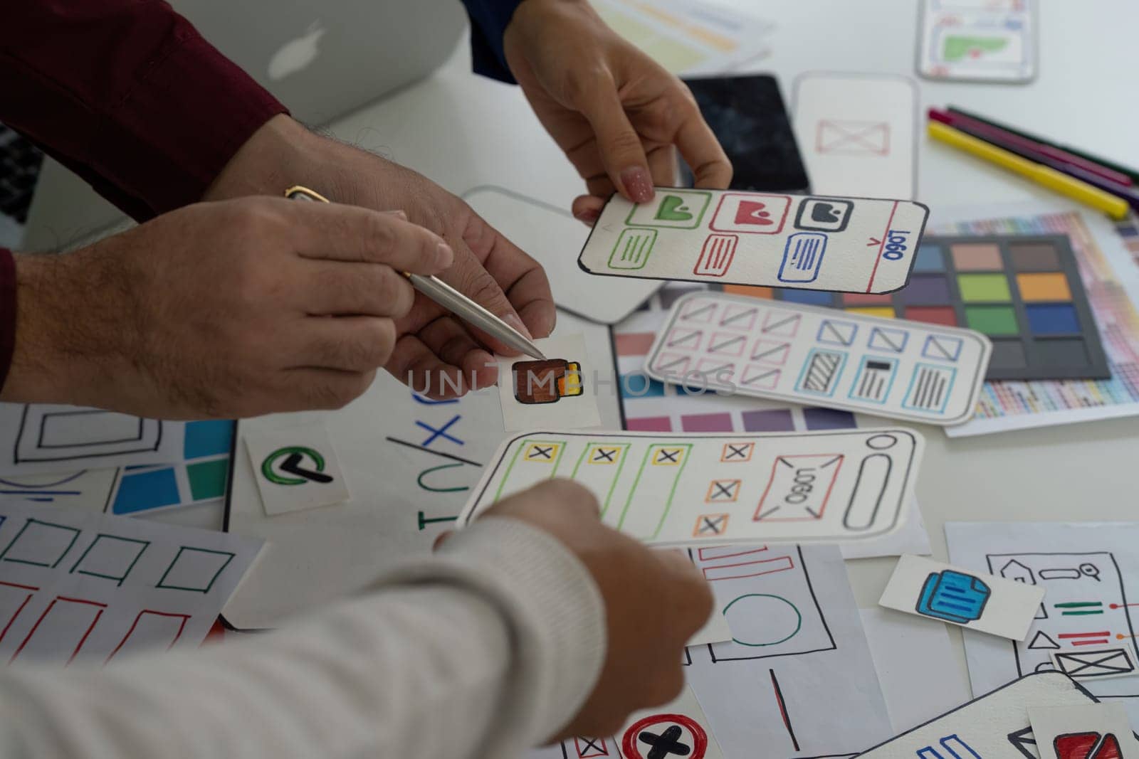 A group of designers collaborates on UX UI concepts, sharing sketches and feedback while holding various design prototypes in hands.