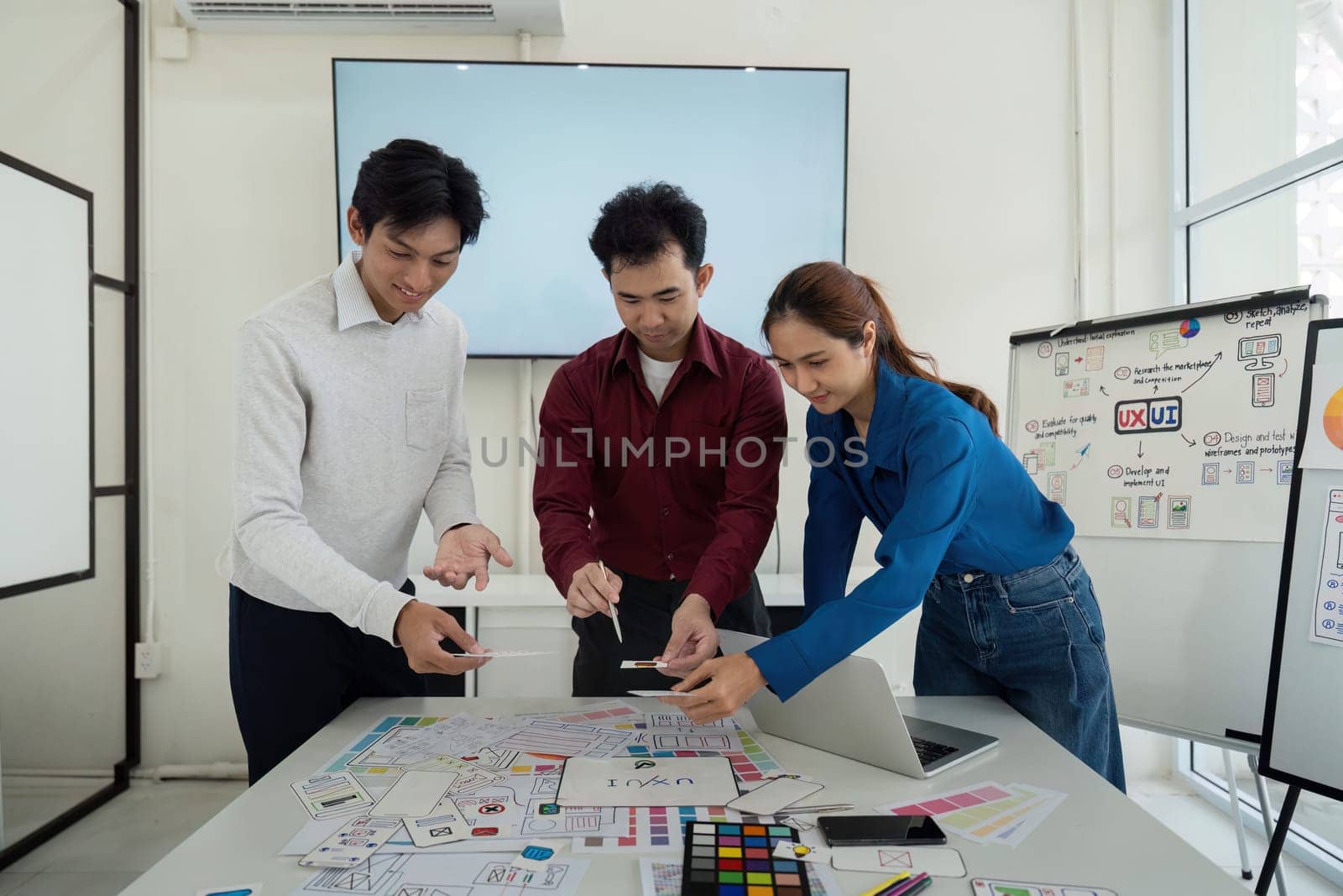 Three designers collaborate on UX solutions, each holding design elements and sketches, actively exchanging ideas to enhance user interface.