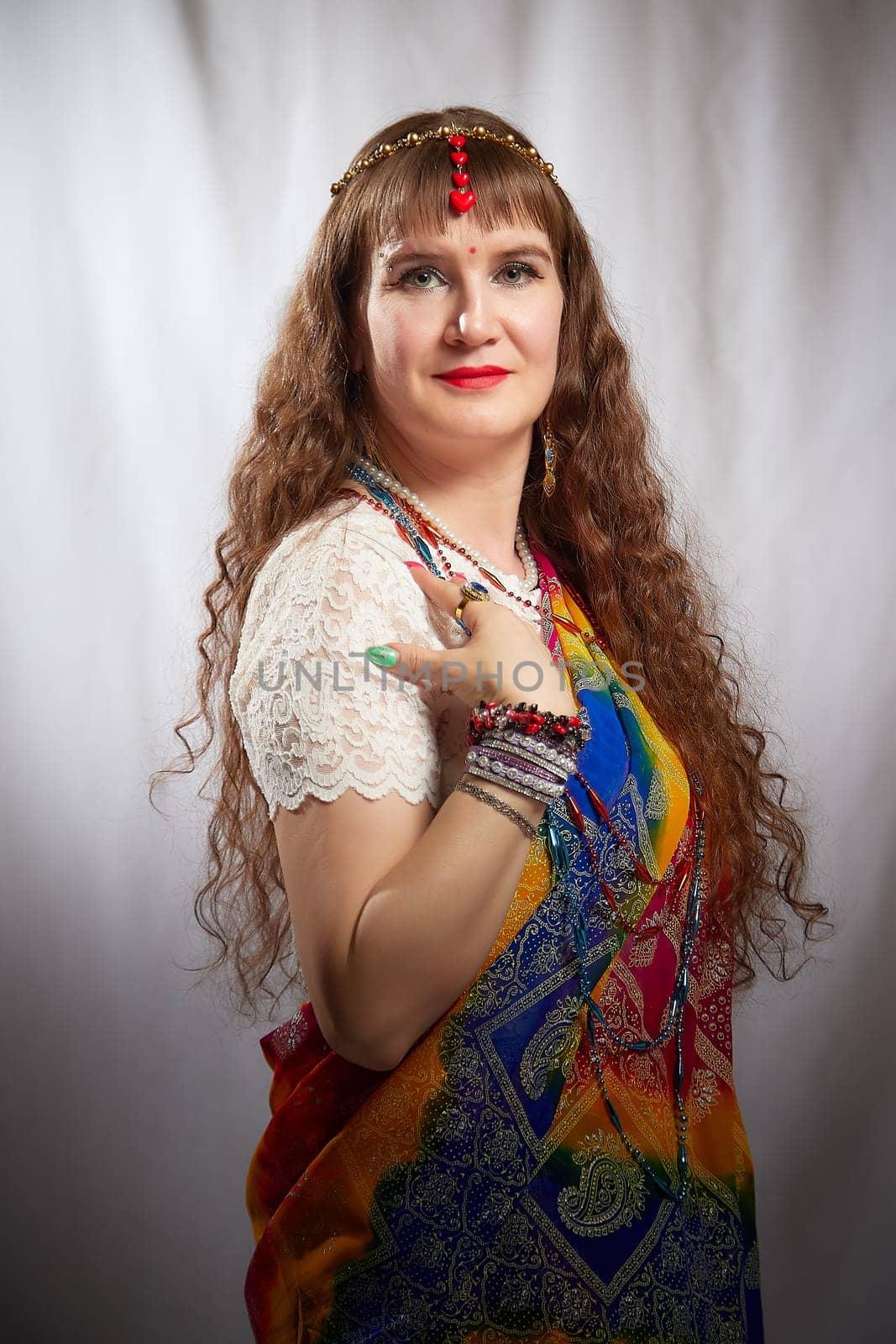 In a creatively lit space, a woman showcases her vibrant sari adorned with jewelry, embodying a blend of heritage and contemporary lifestyle.