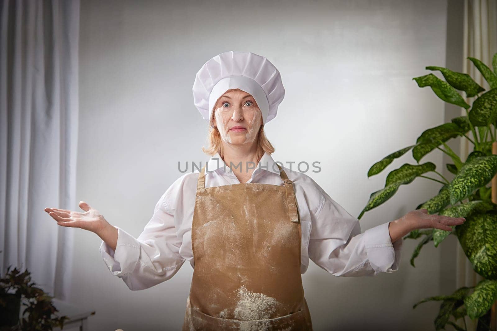 A funny photo shoot captures an elderly woman chef joyfully showcasing flour while cooking in her cozy kitchen.